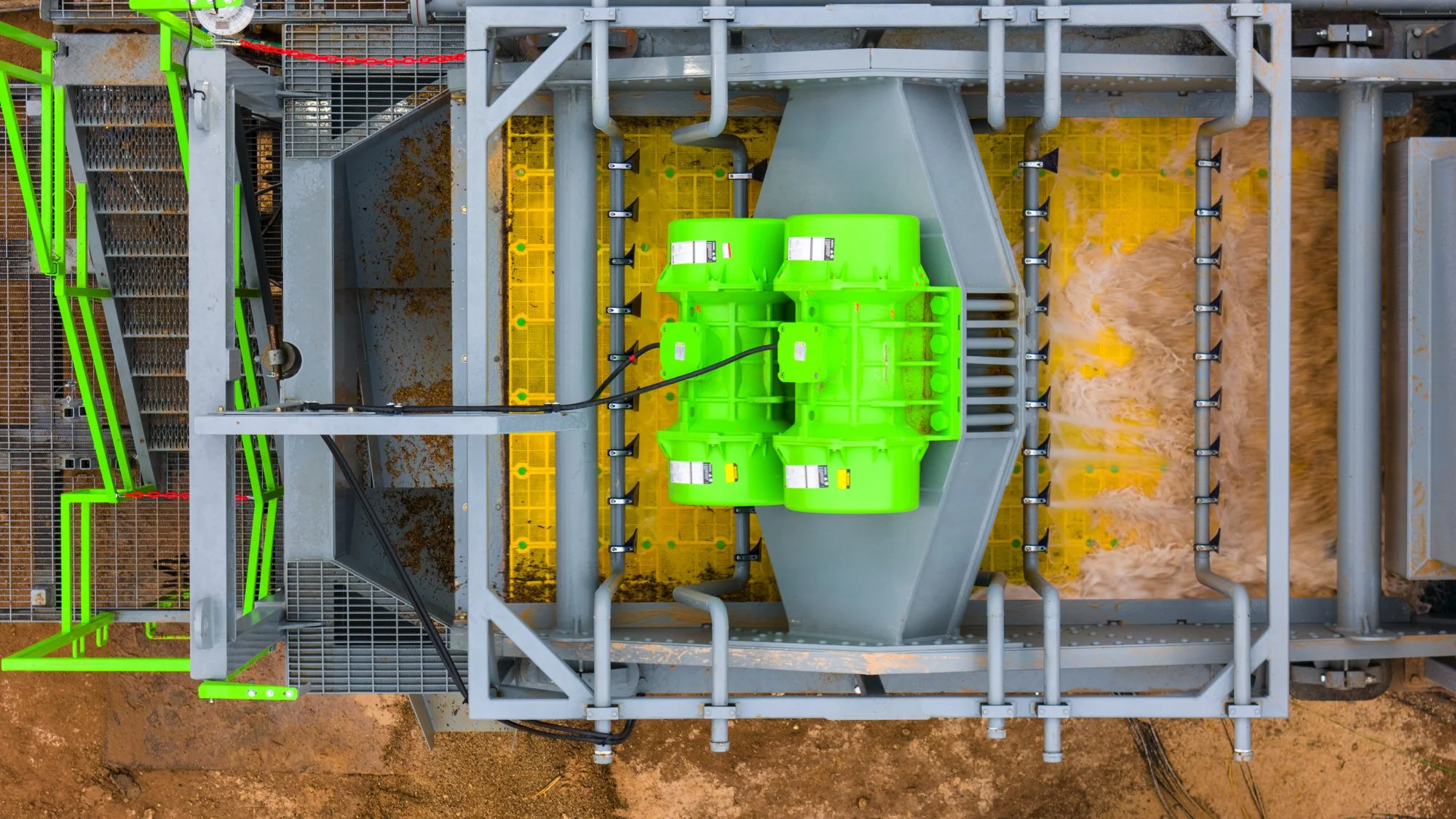 Top-down view of an industrial water treatment tank with gray and green components, yellow grids, and piping systems, set on a dirt ground.