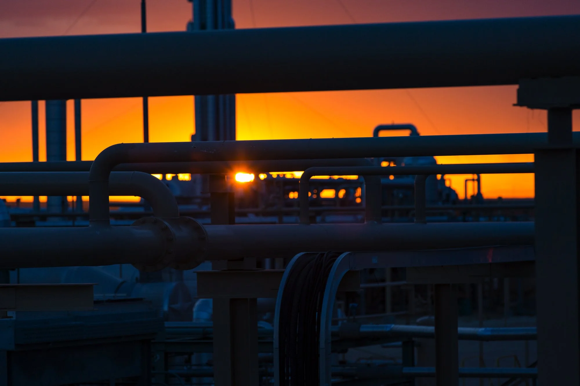 Industrial pipes and structures silhouetted against a sunset sky.