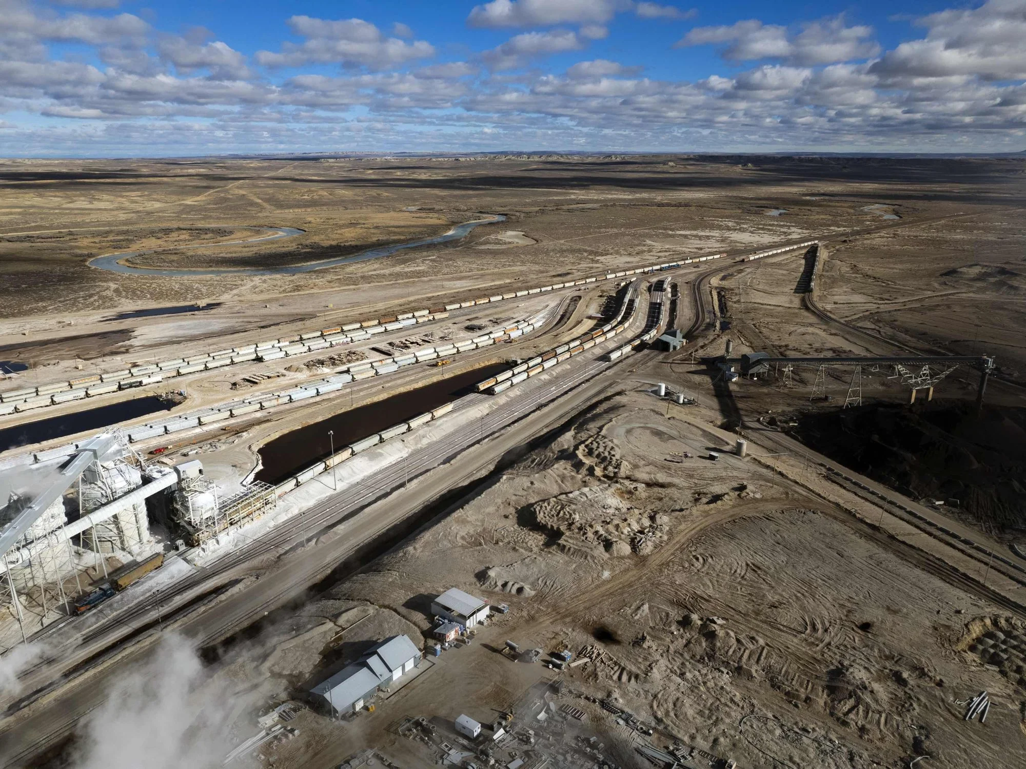 Aerial view of a train yard in a desert landscape with multiple train tracks, trains, and industrial structures.