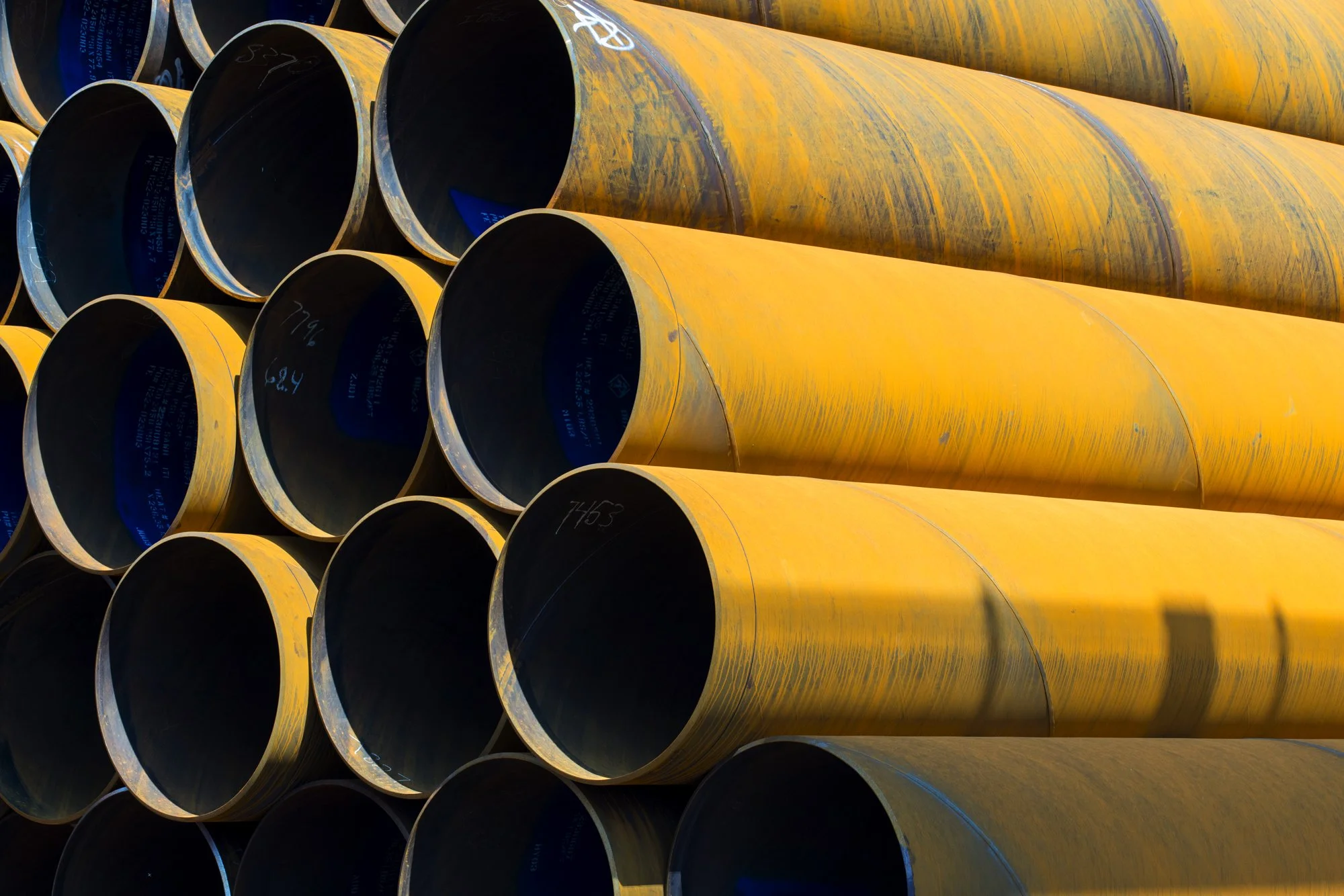 Stacked yellow and black industrial pipes in a construction yard.