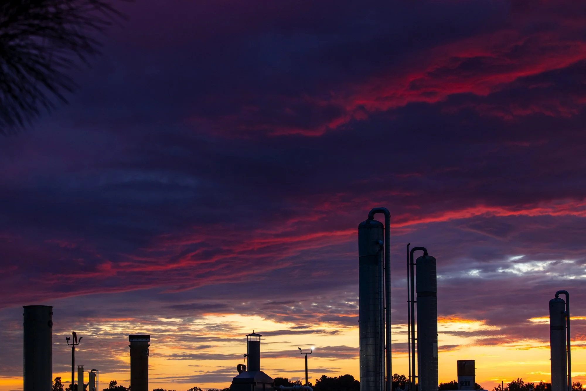 Industrial pipes and chimneys silhouetted against a colorful sunset sky with clouds.