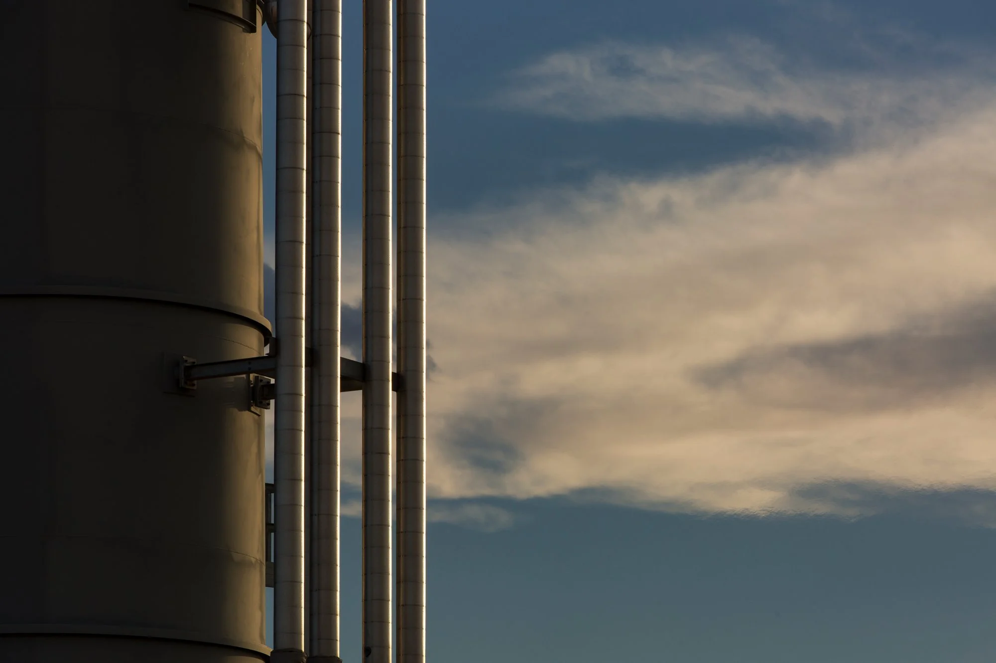 Industrial pipes and a large cylindrical structure against a cloudy sky.