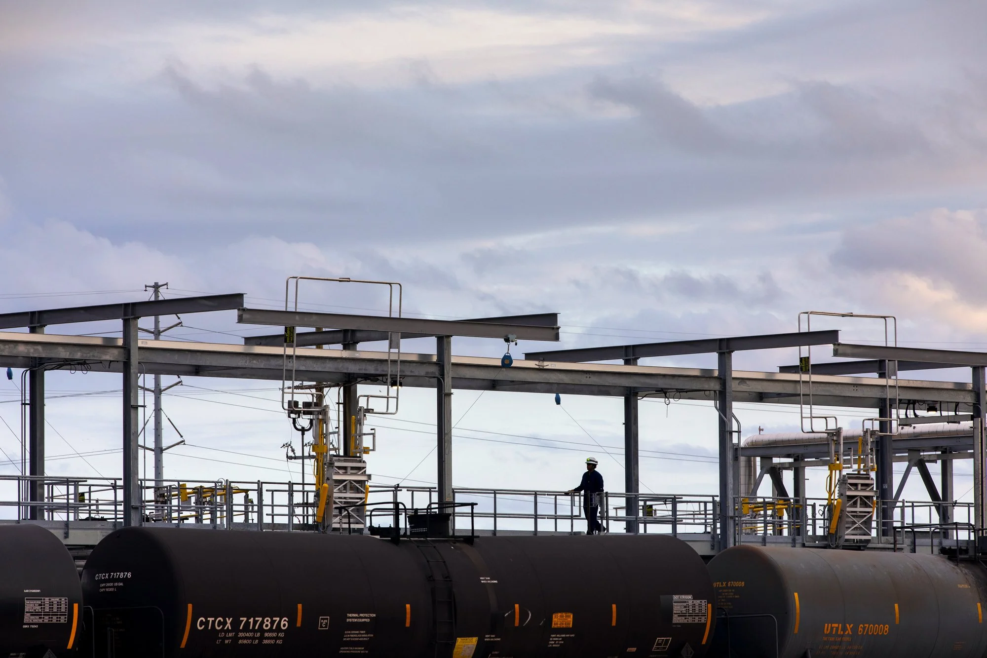 A worker standing on an industrial oil storage tank facility under a cloudy sky.