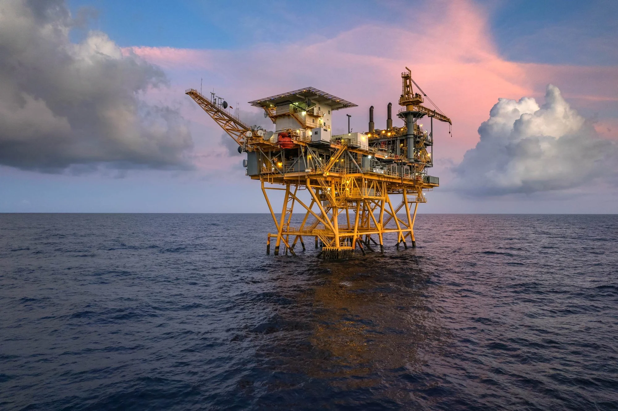 An offshore oil rig in the ocean during sunset with clouds in the sky.