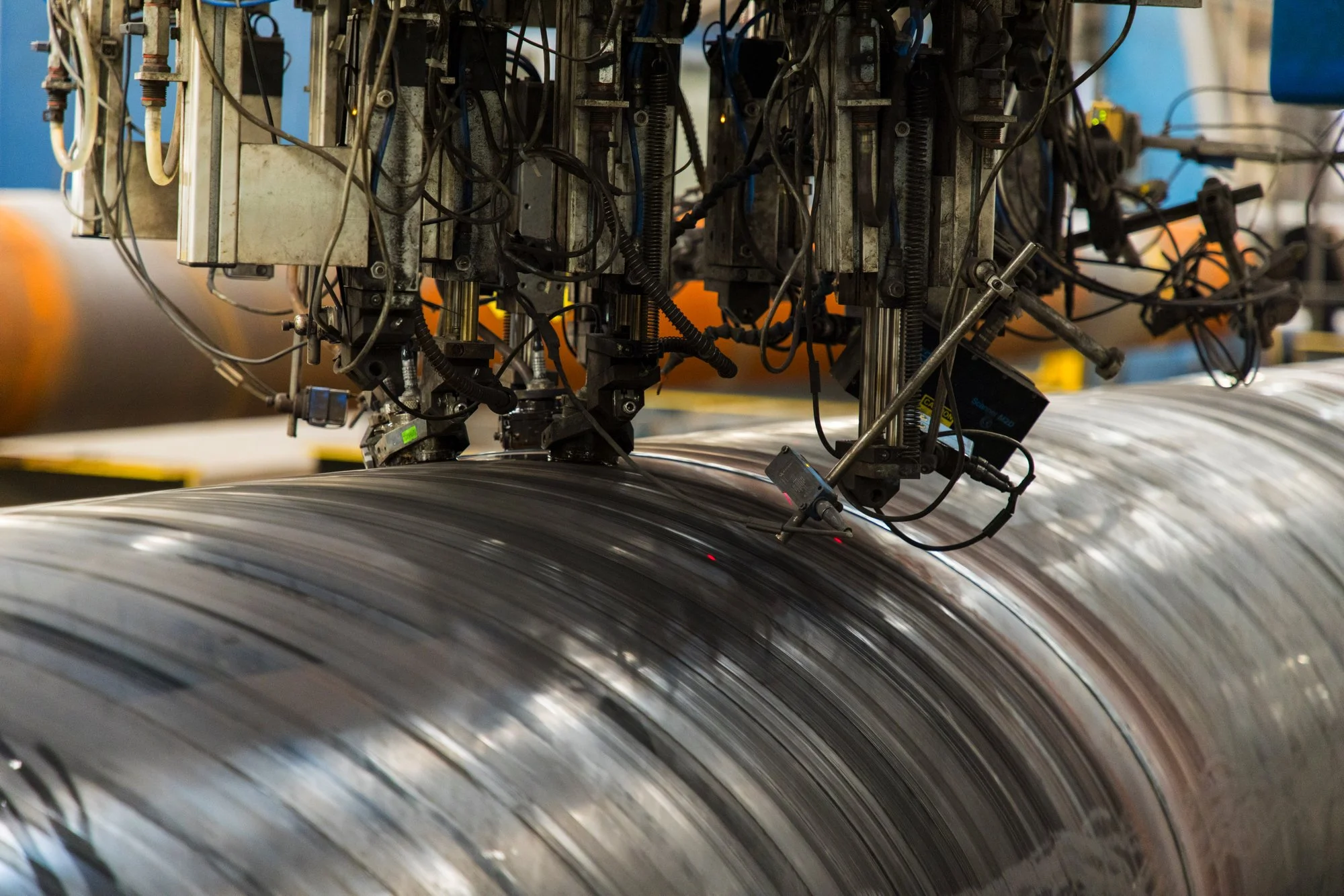Close-up of industrial machinery inspecting or manufacturing a large metal pipe in a factory setting.