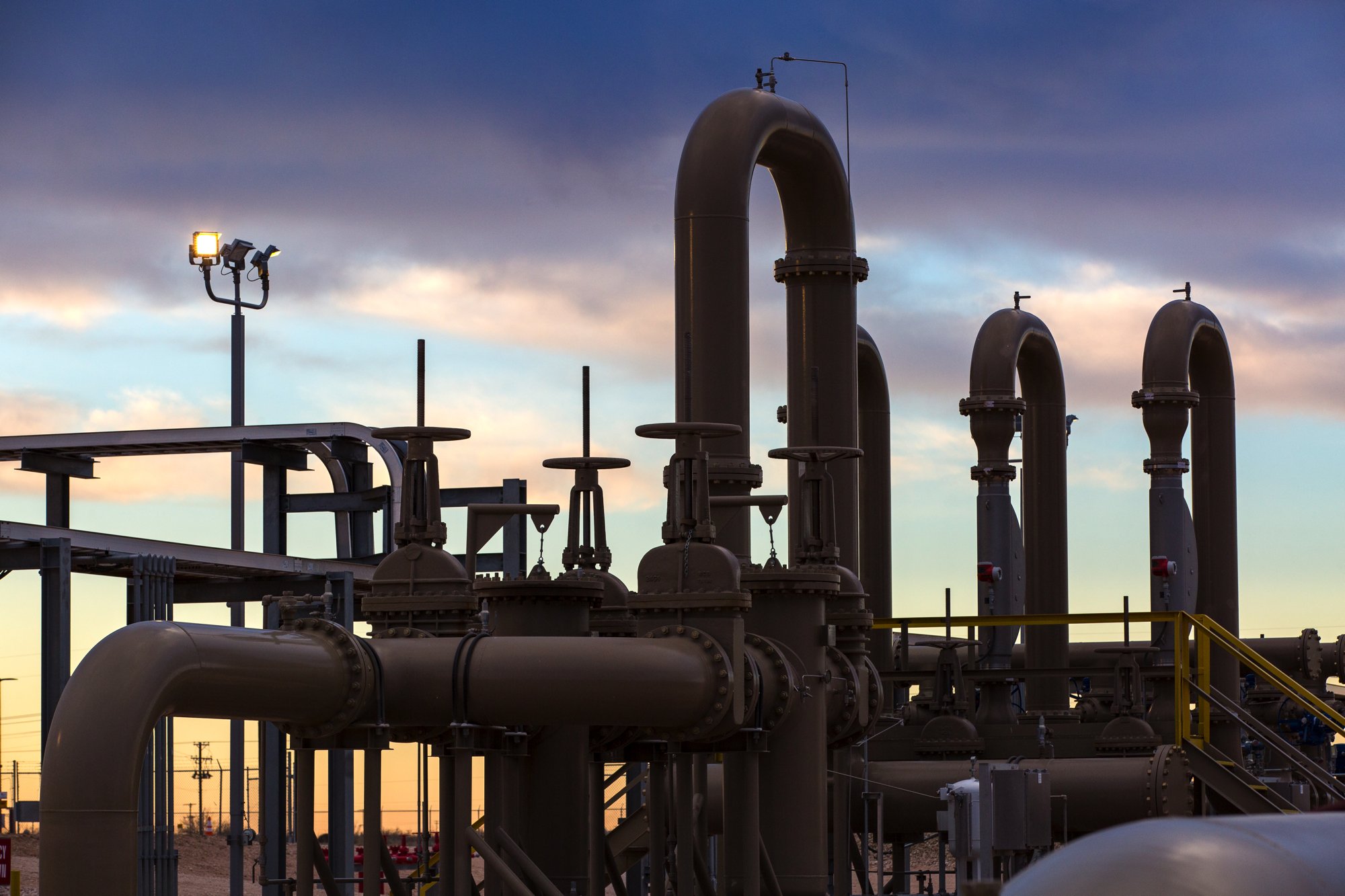 Industrial pipes and infrastructure against a cloudy sunset sky.