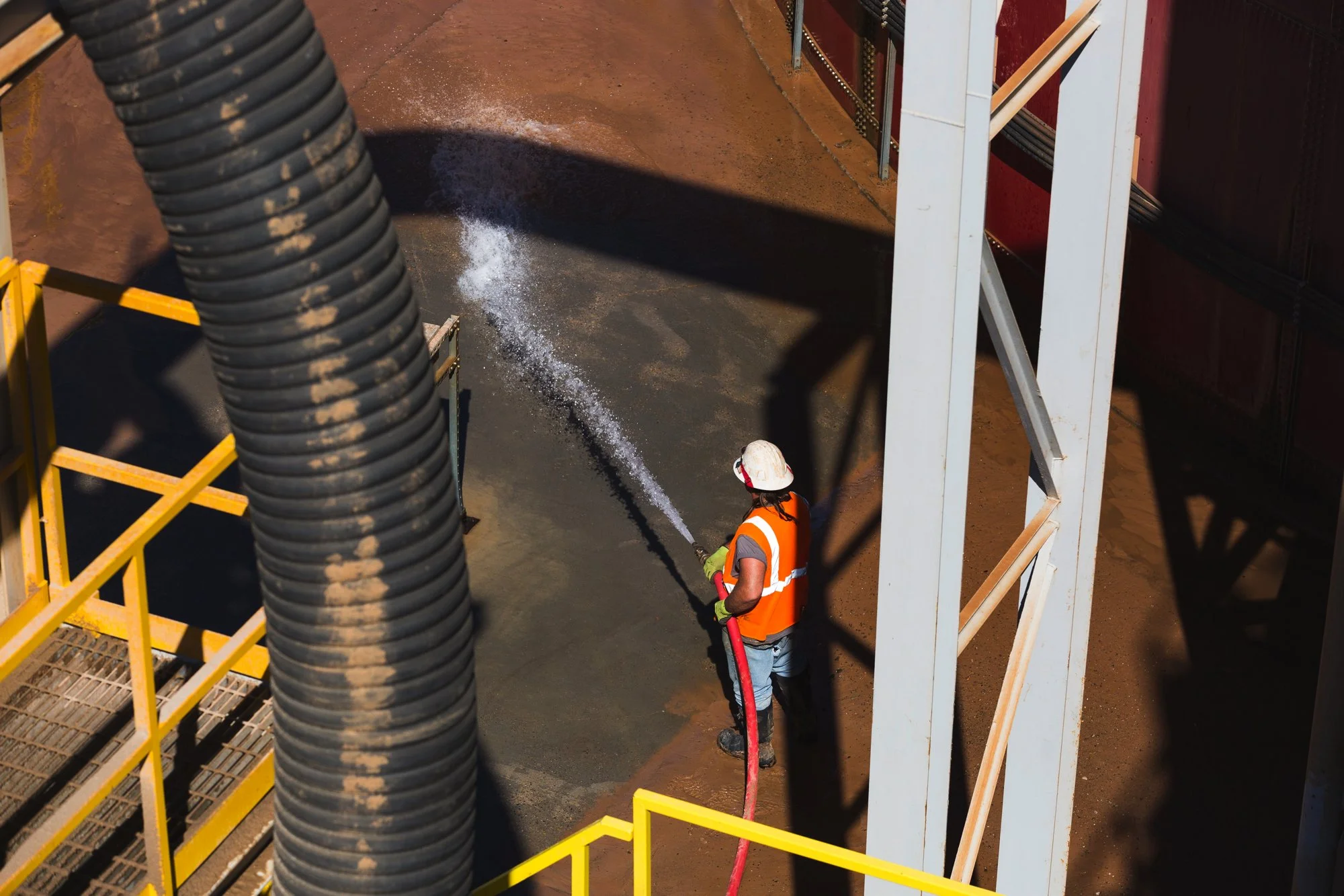 Worker wearing safety gear power washing a concrete surface at an industrial site.