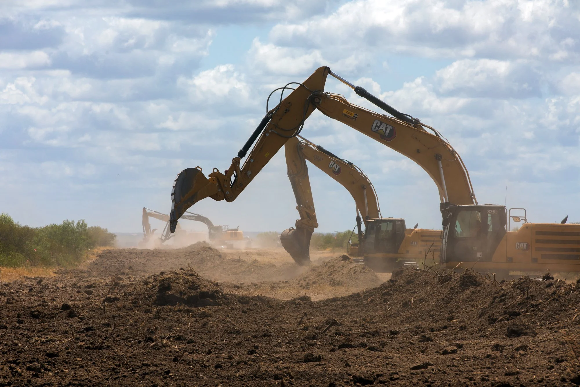 Construction site with multiple large excavators working on dirt, under a partly cloudy sky.