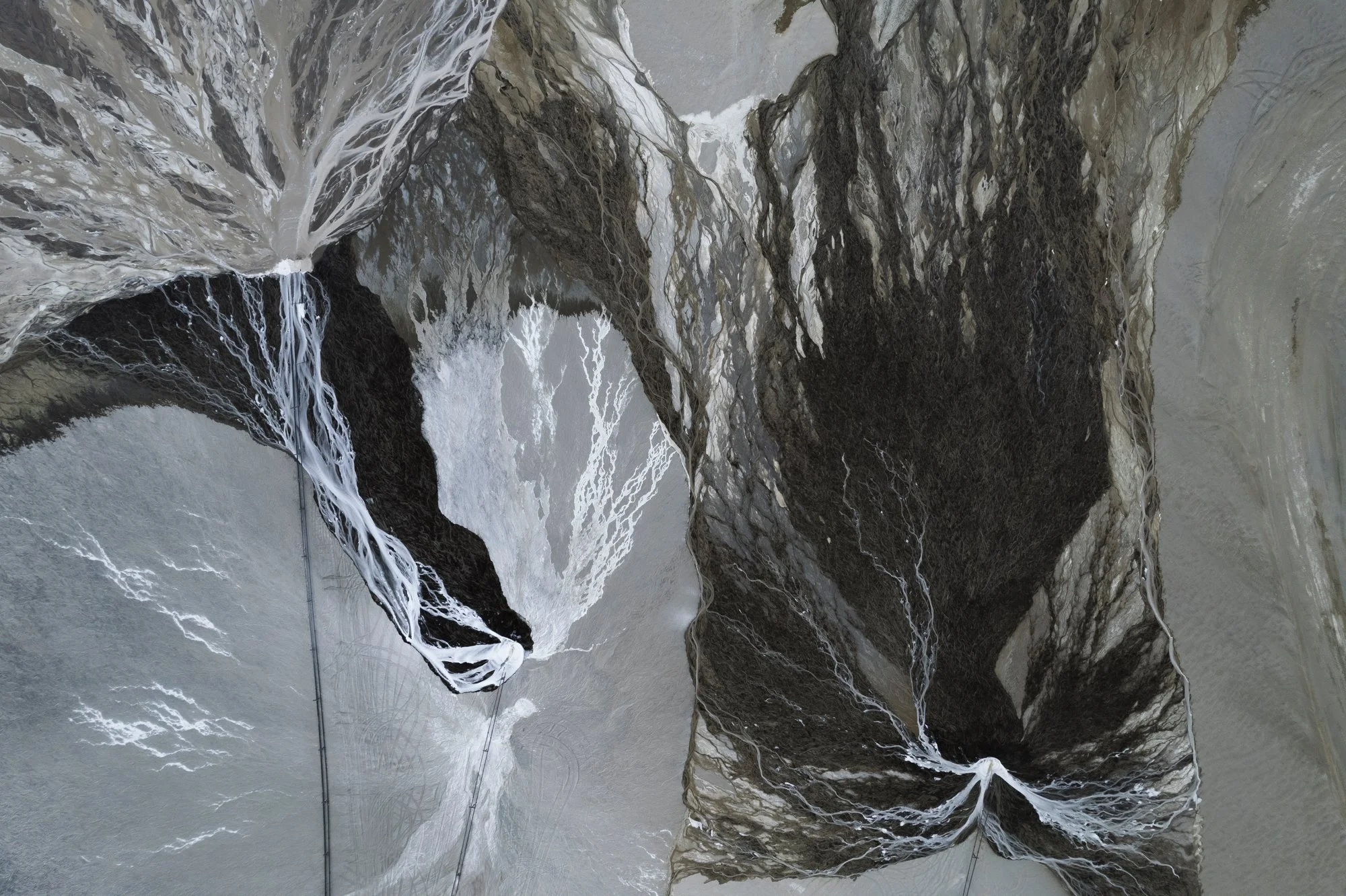 Aerial view of a canyon with a river running through, surrounded by tall cliffs with paths or bridges across the canyon.