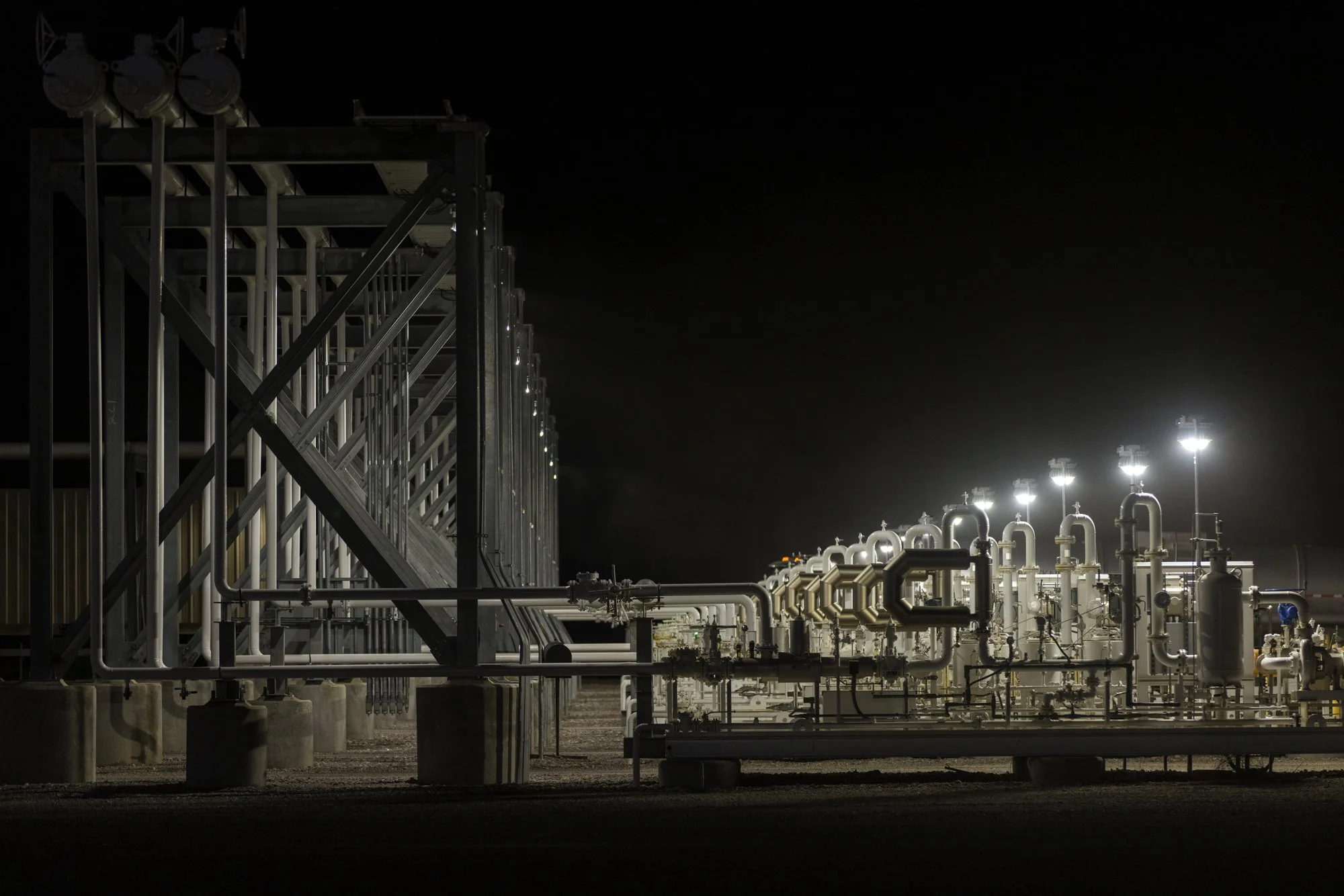 Industrial facility at night with illuminated pipelines and equipment.