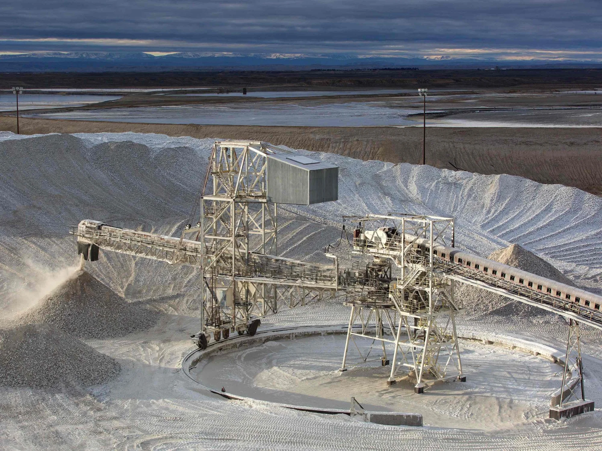 A salt mining operation with large machinery extracting salt from a salt flat under a cloudy sky.