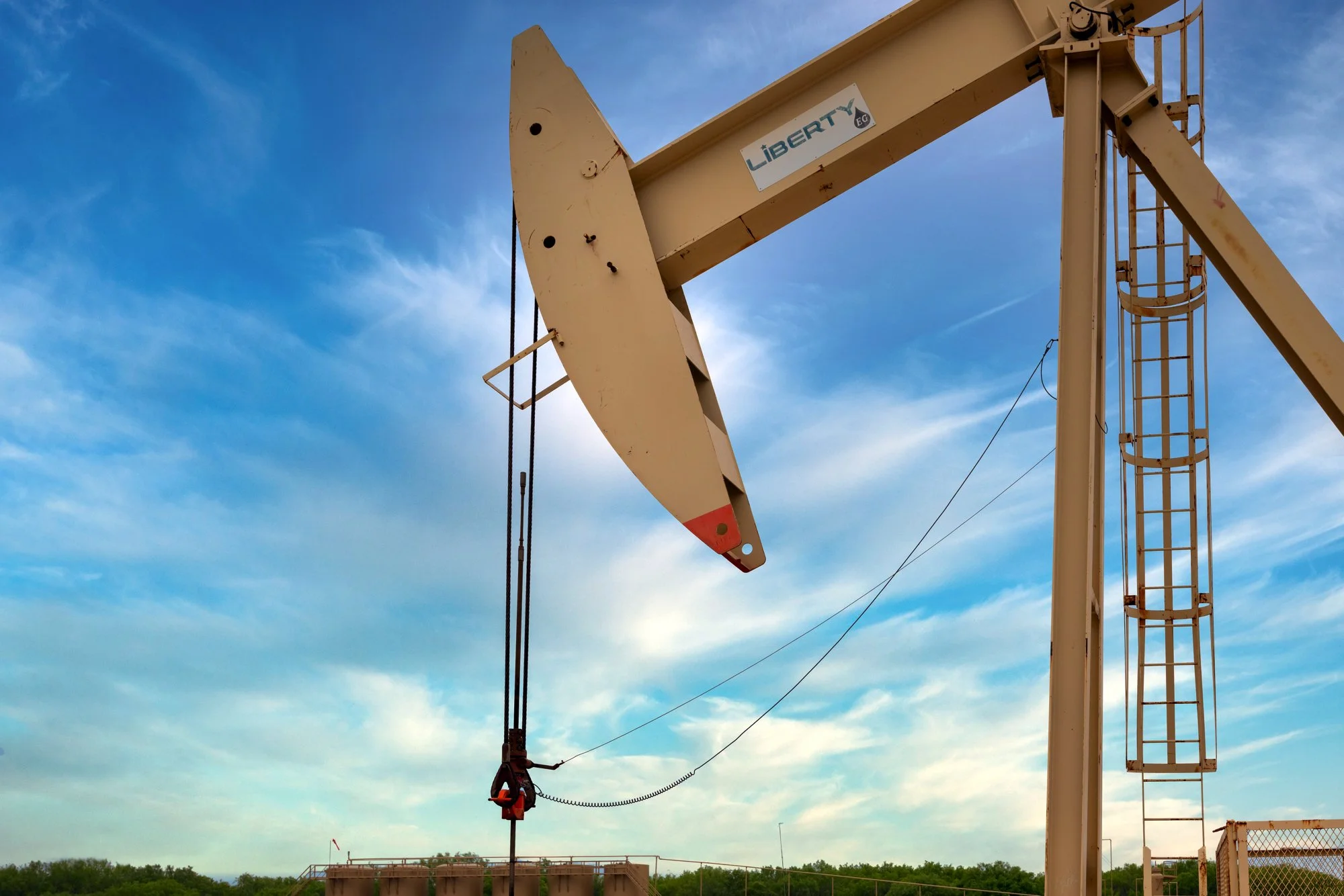 Oil pumpjack operating under a blue sky with some clouds.