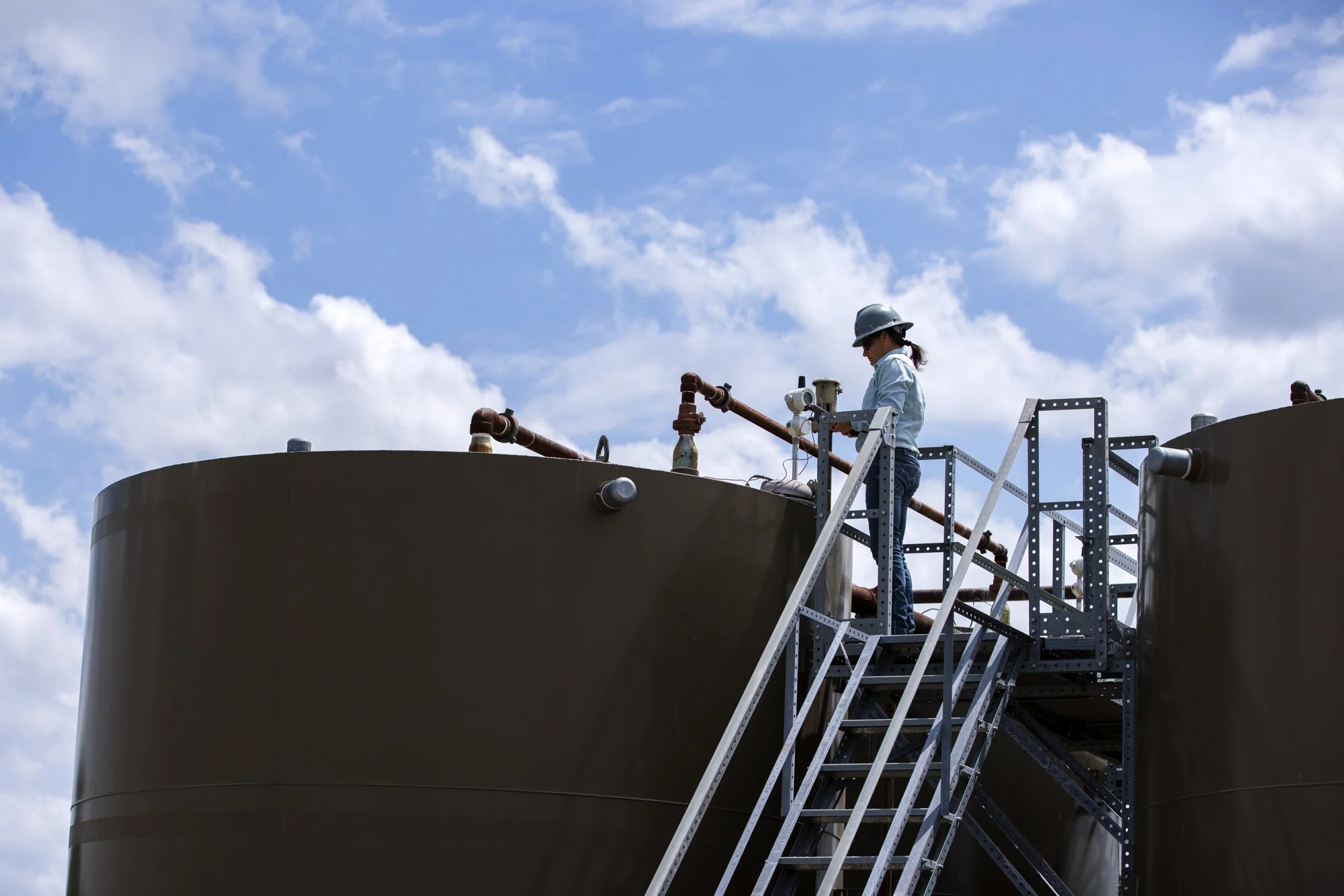 A woman in safety gear inspecting industrial tanks outdoors.