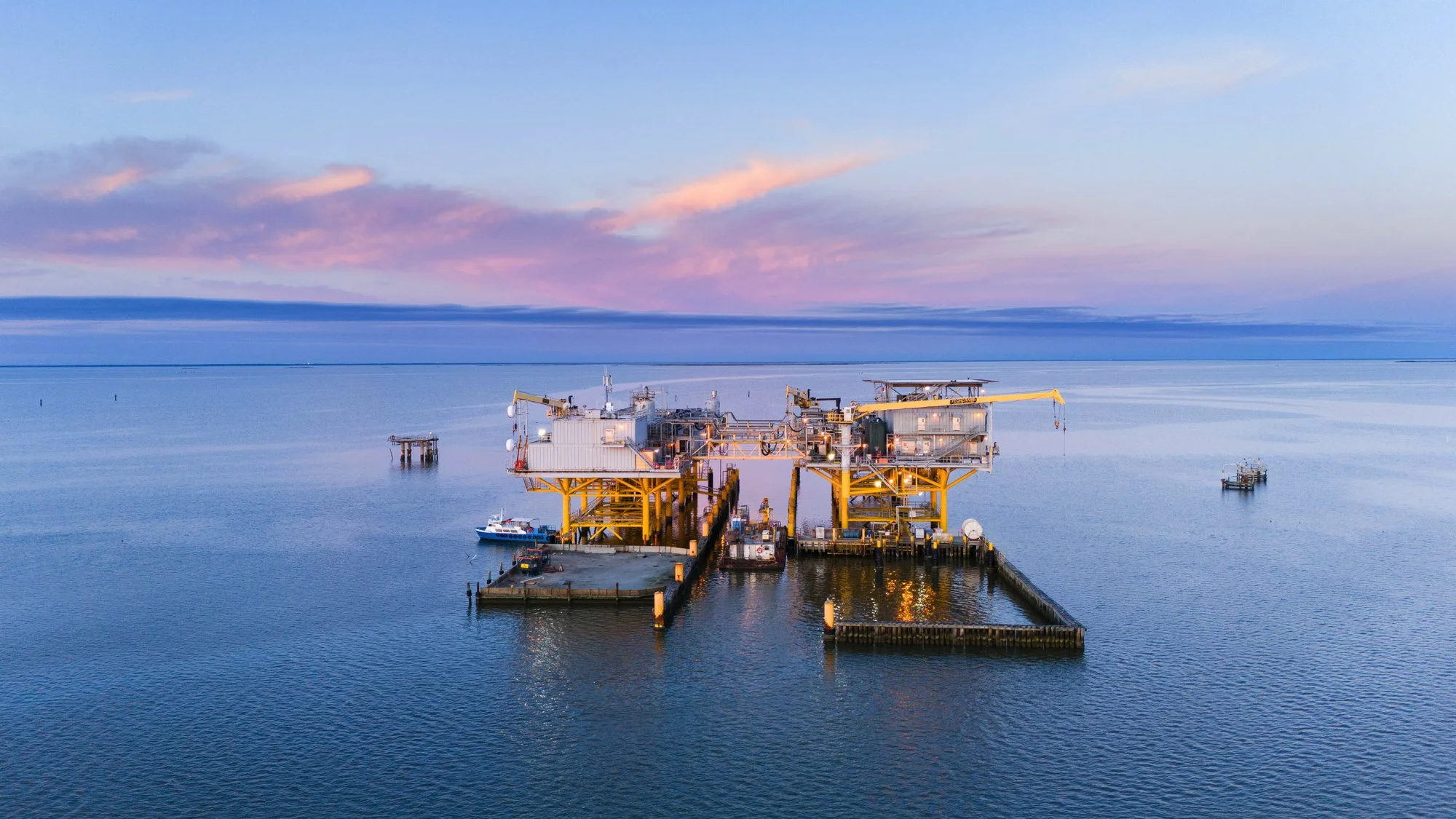 An offshore oil platform in calm ocean waters during sunset or sunrise.