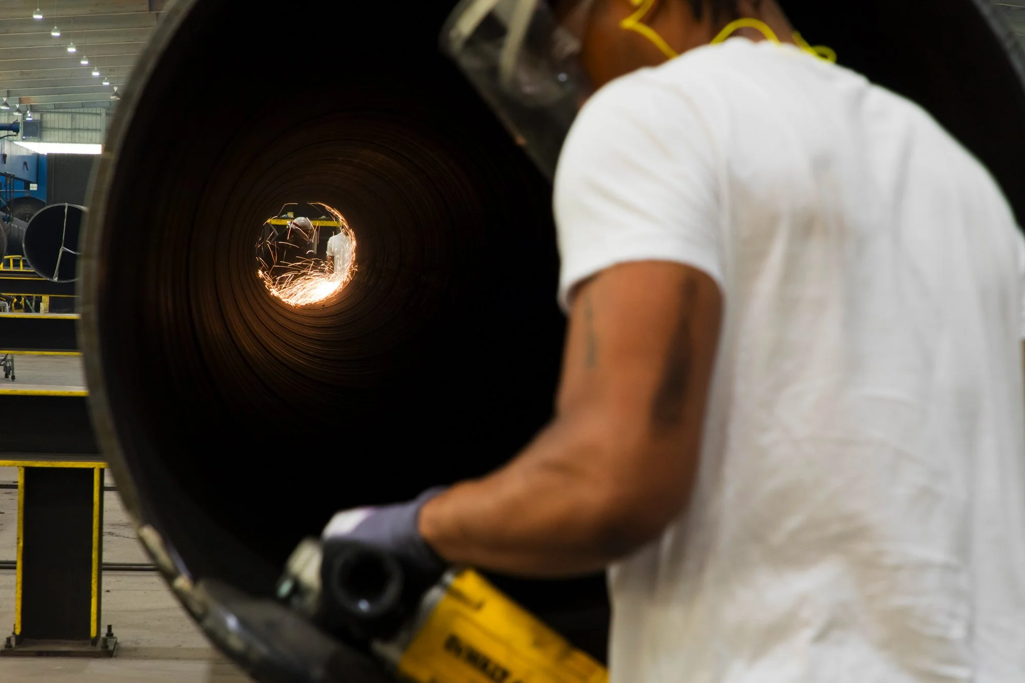Worker welding a large metal pipe in an industrial workshop.