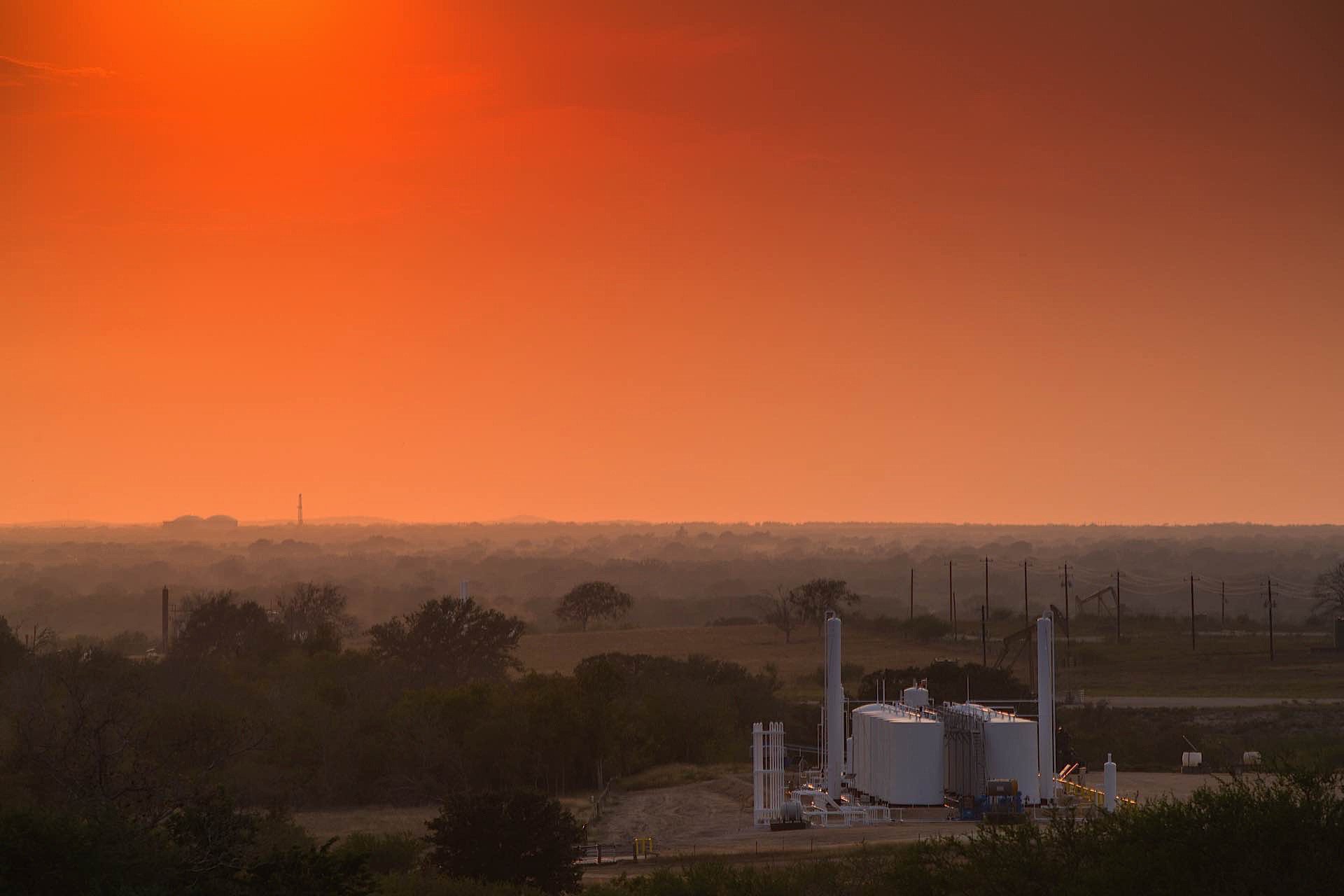 A large rocket on a launchpad surrounded by trees and natural landscape, with a vibrant orange sunset or sunrise sky in the background.
