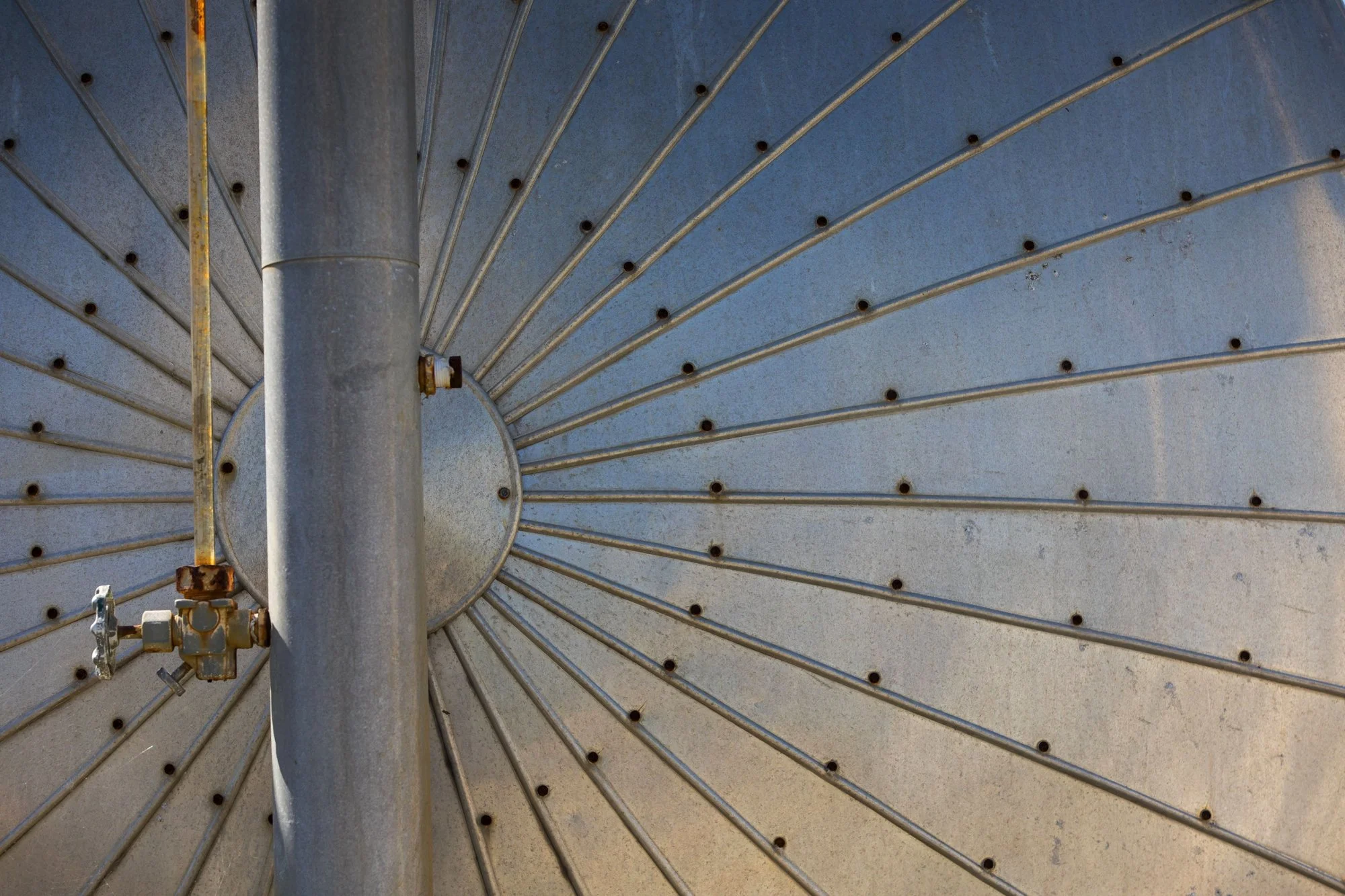 Close-up of a metallic satellite dish with a central pole and evenly spaced rivets or screws, viewed from underneath.