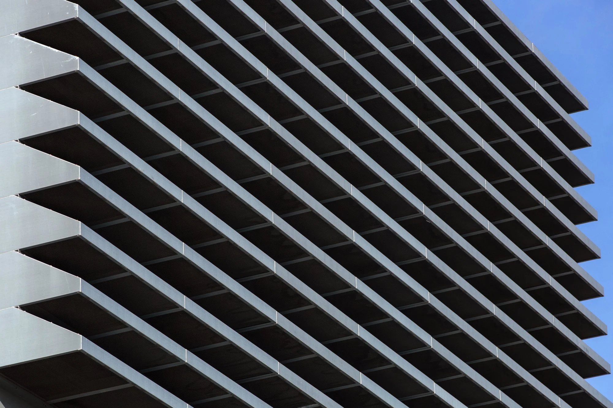 Close-up view of a modern multi-story building with horizontal lines and dark balcony railings, against a clear blue sky.