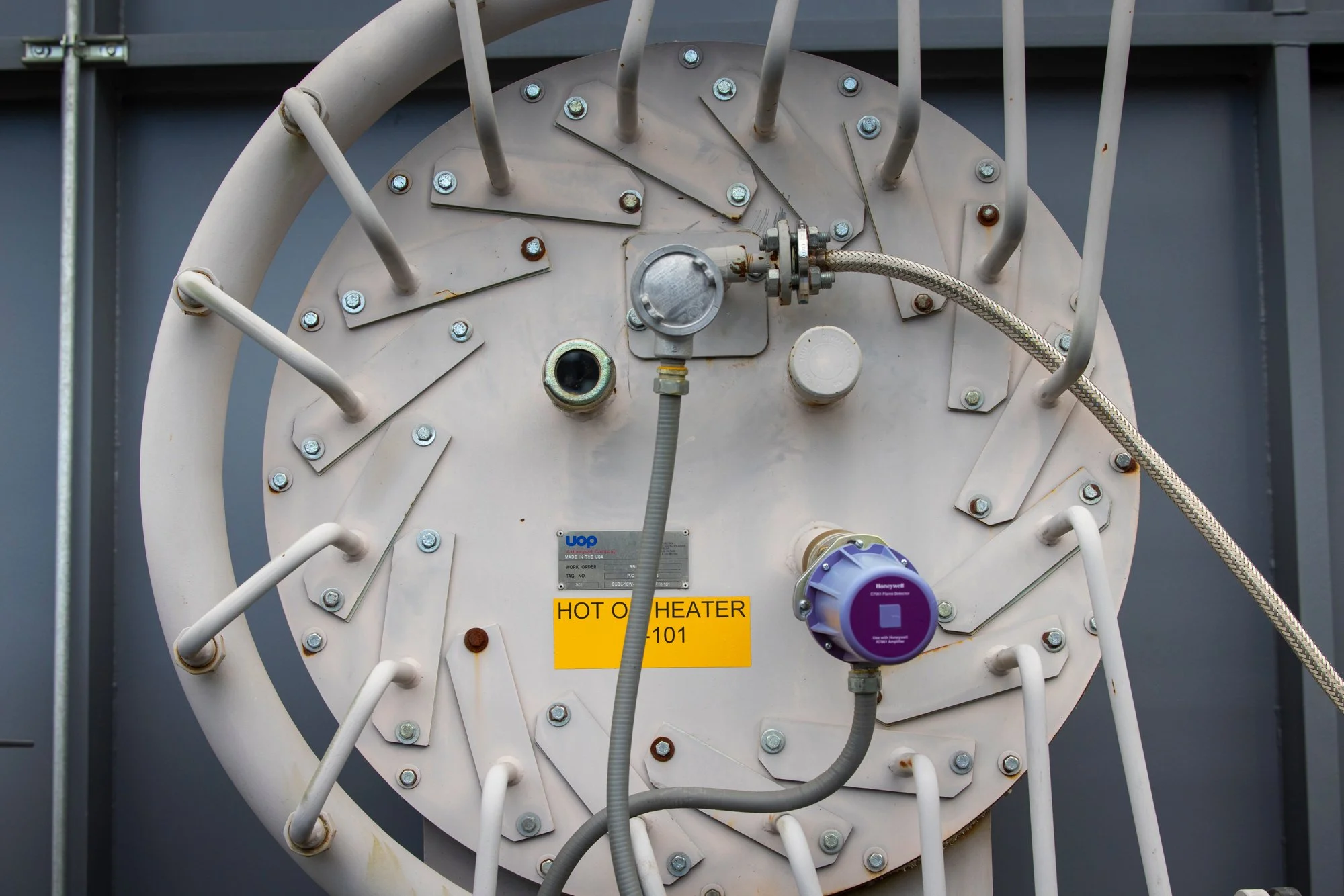 Close-up of a large industrial heater with various pipes, gauges, and labels, including a yellow sign that reads 'HOT O HEATER 101'.