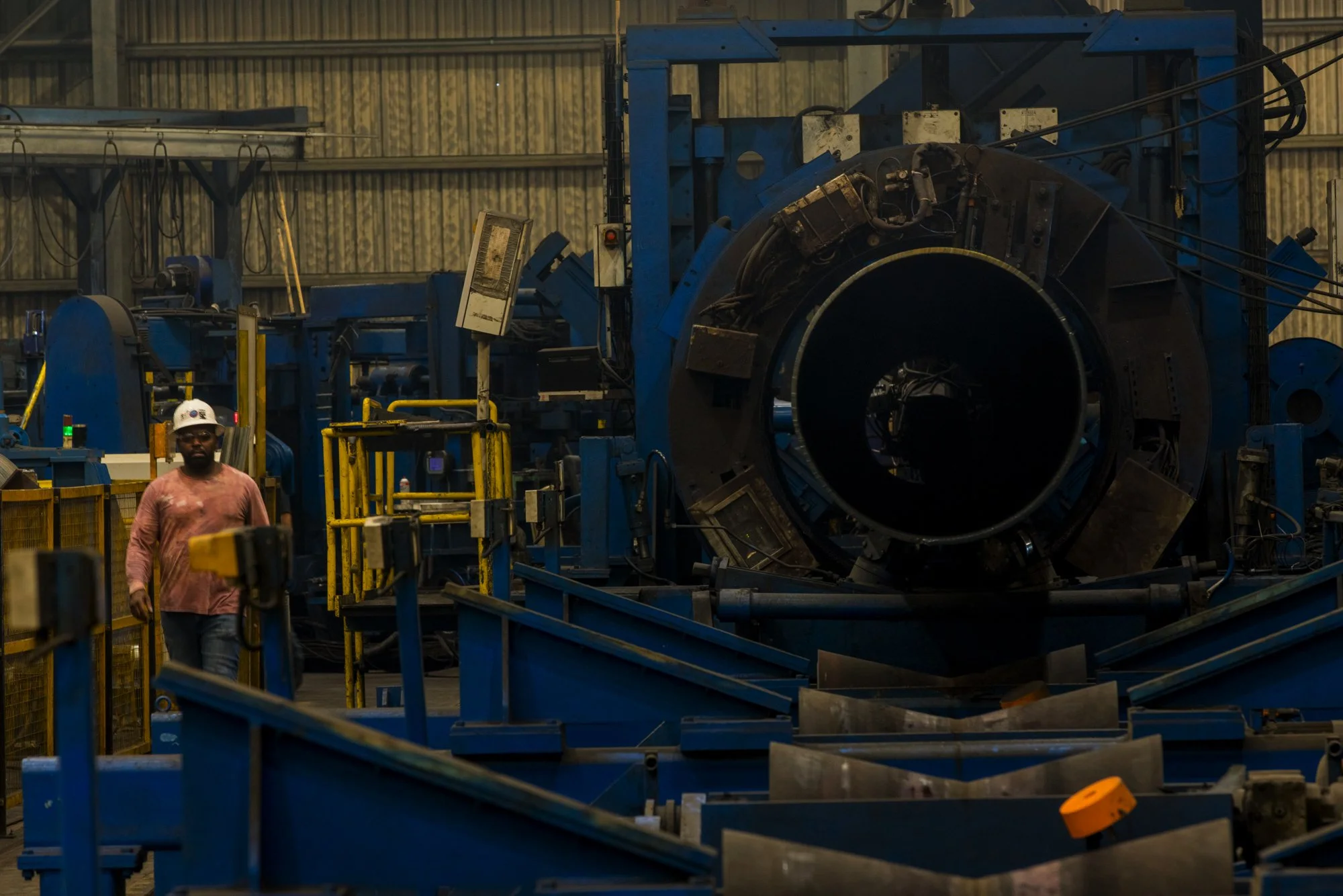 A worker walking in a factory with large blue industrial machinery and equipment.