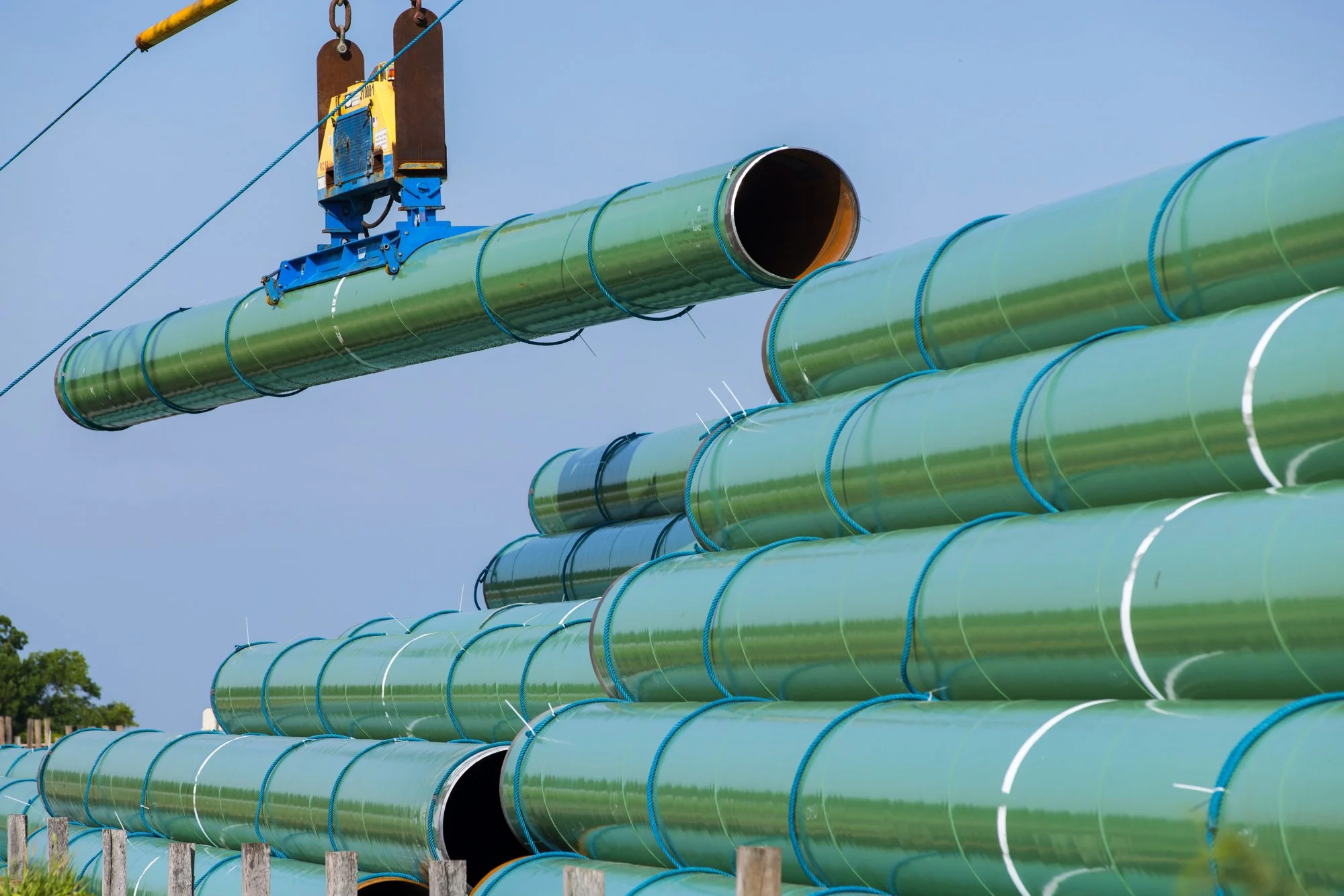 Large green pipelines being installed or assembled outdoors, with one pipe being held by a crane or lifting device.
