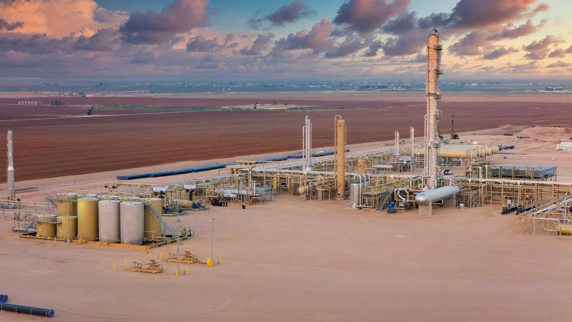A large oil refinery with multiple storage tanks, pipelines, and processing towers situated in a desert landscape.