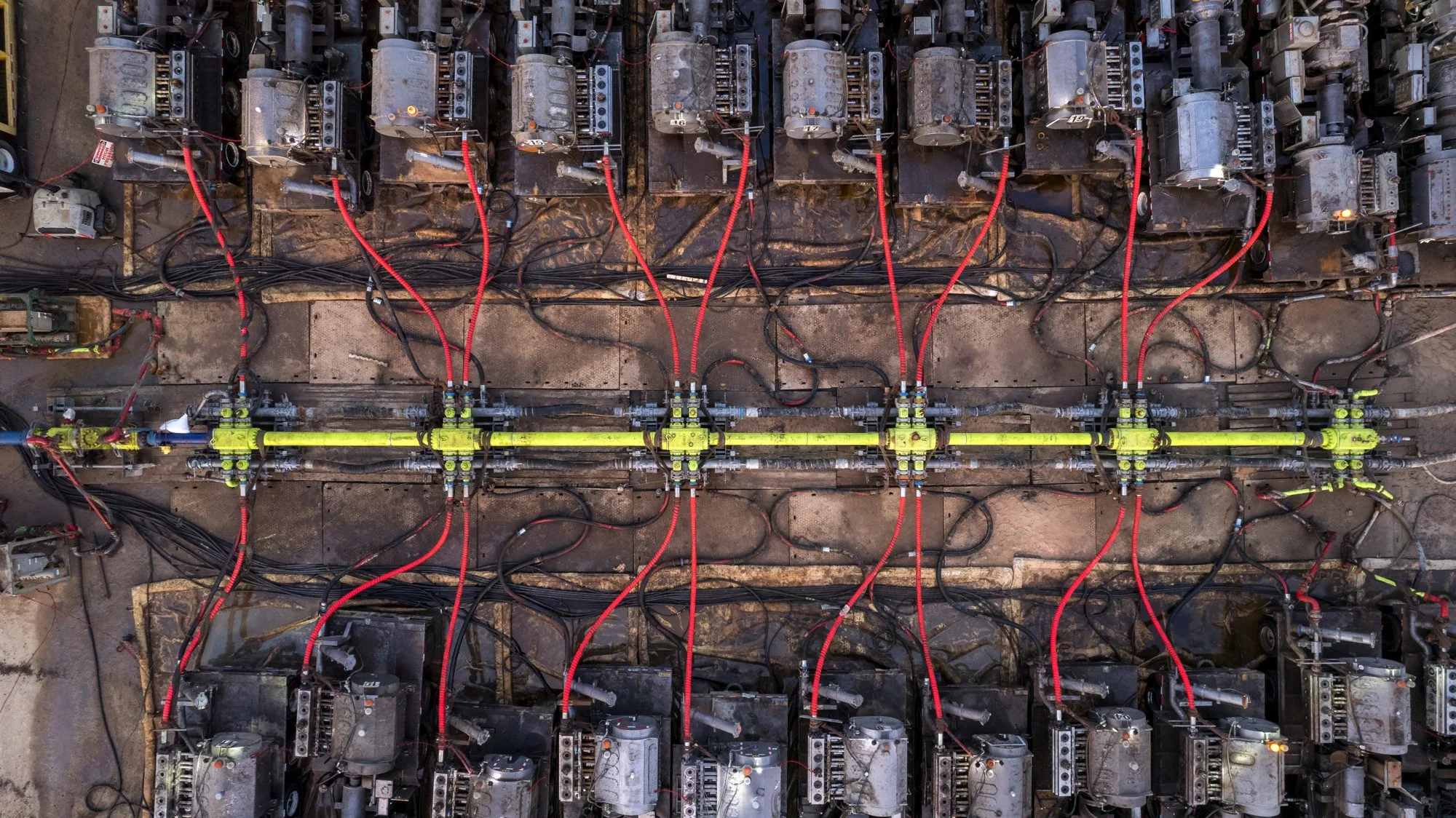 An aerial view of a large industrial machine setup with motors, red and black cables, and pipes on a concrete floor.