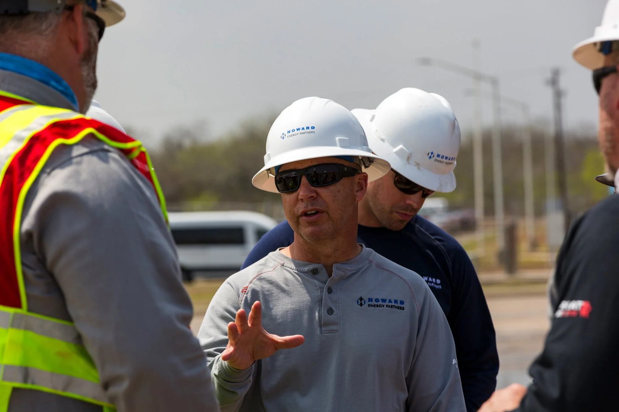 Group of construction workers wearing safety helmets and sunglasses having a discussion outdoors.