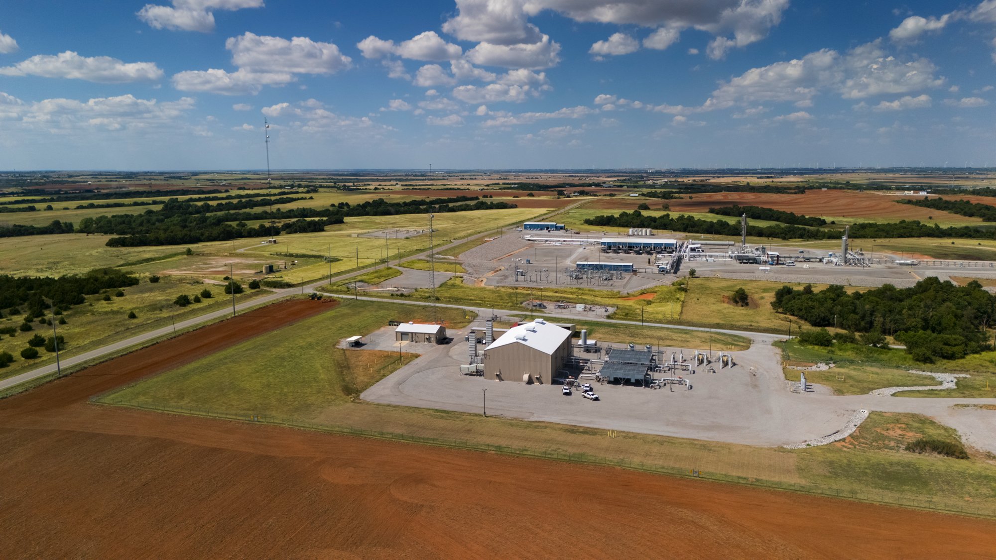 Aerial view of a power plant surrounded by fields and farmland under a blue sky with clouds.
