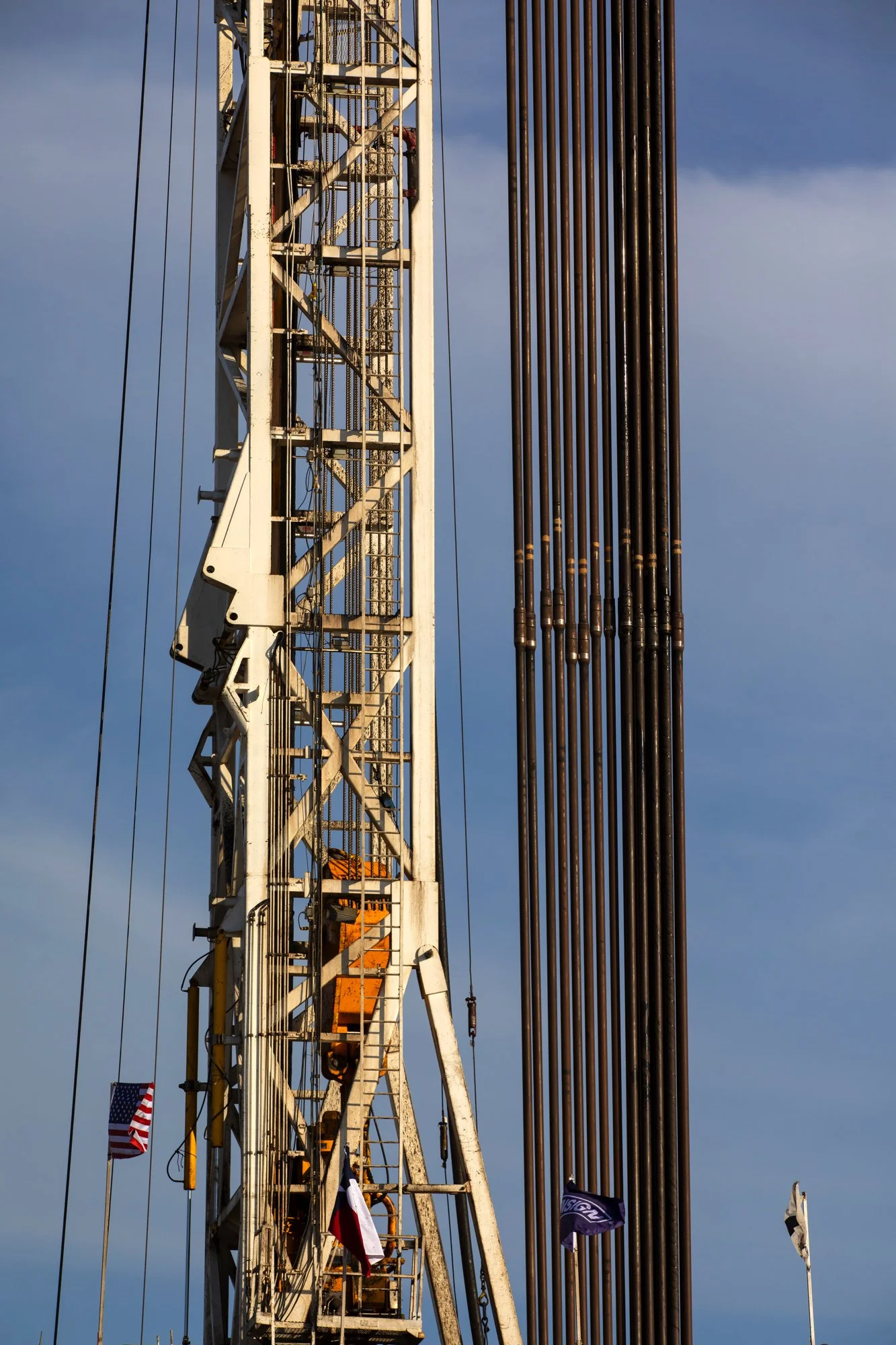 Close-up of a large oil or gas drilling rig against a partly cloudy sky, with flags flying at the bottom.