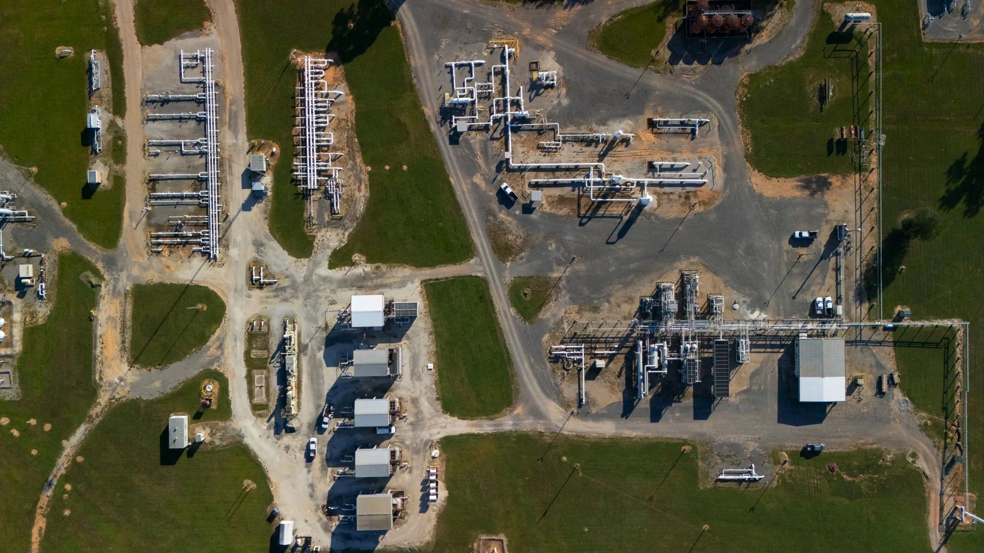 Aerial view of an electrical substation with transformers, power lines, and green grassy areas.