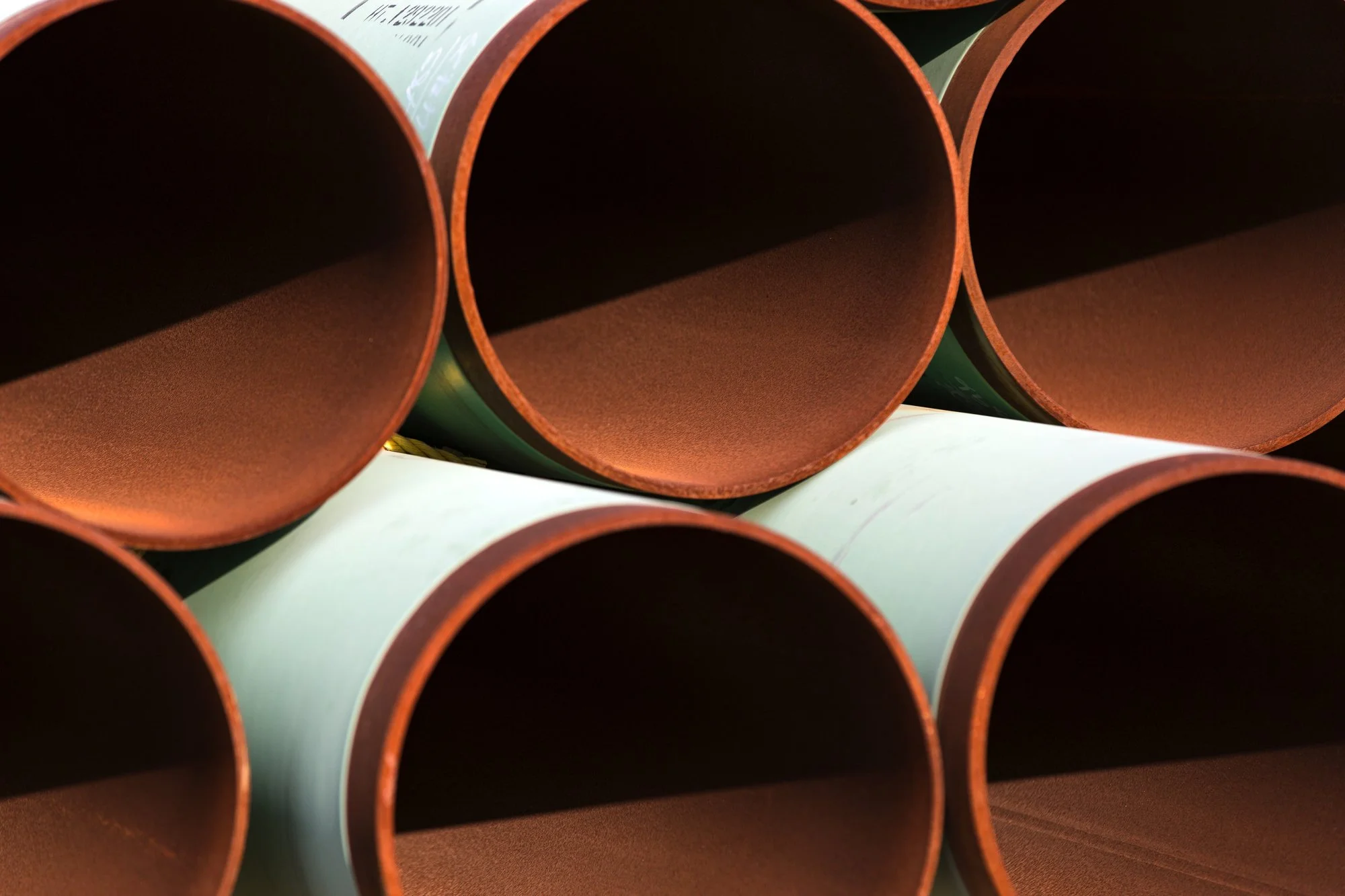 A close-up view of stacked brown and light blue cylindrical pipes stored in a horizontal position.