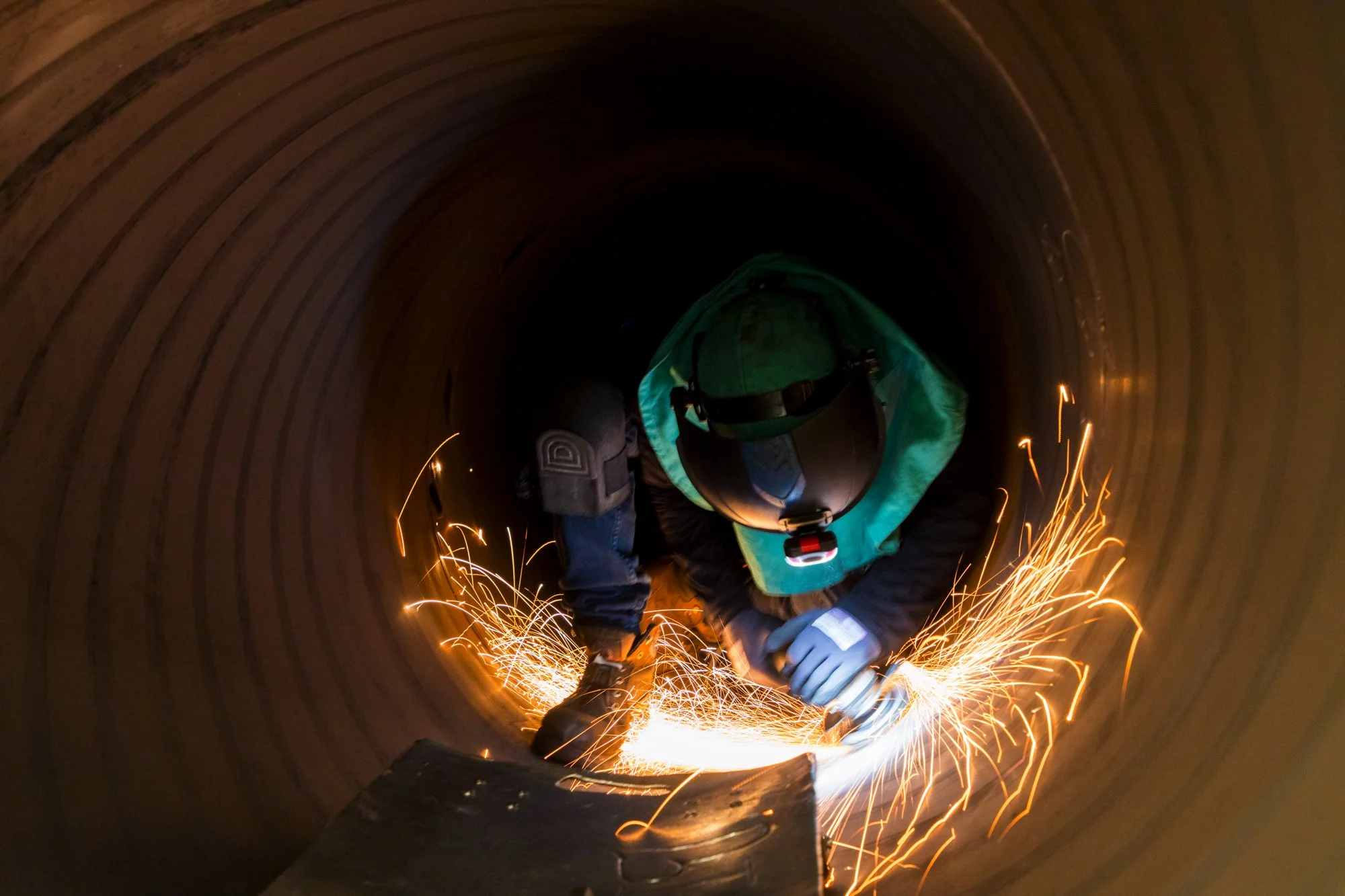 Worker welding inside a large metal pipe, with bright sparks flying around.