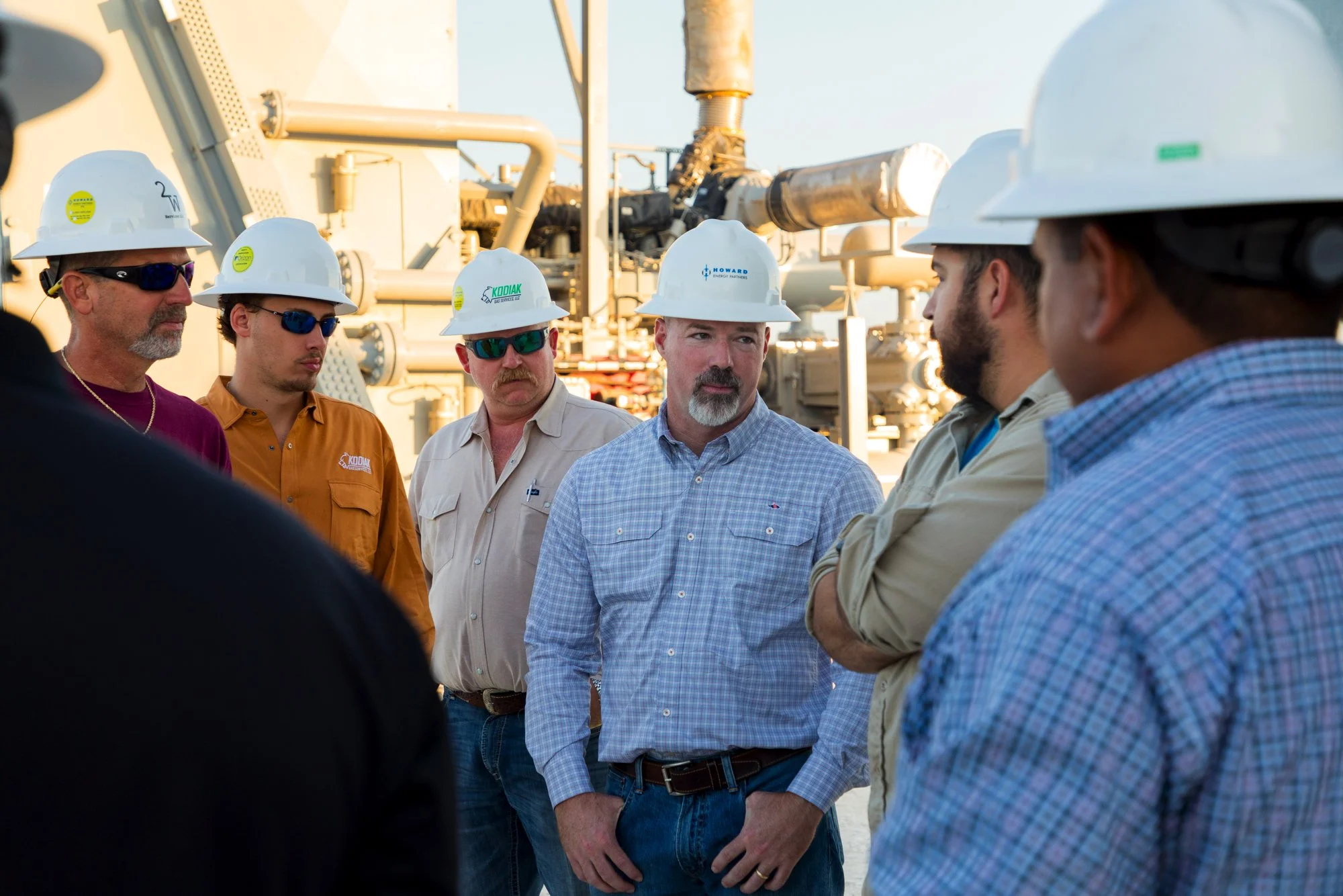 Group of workers wearing hard hats having a discussion outdoors near industrial equipment