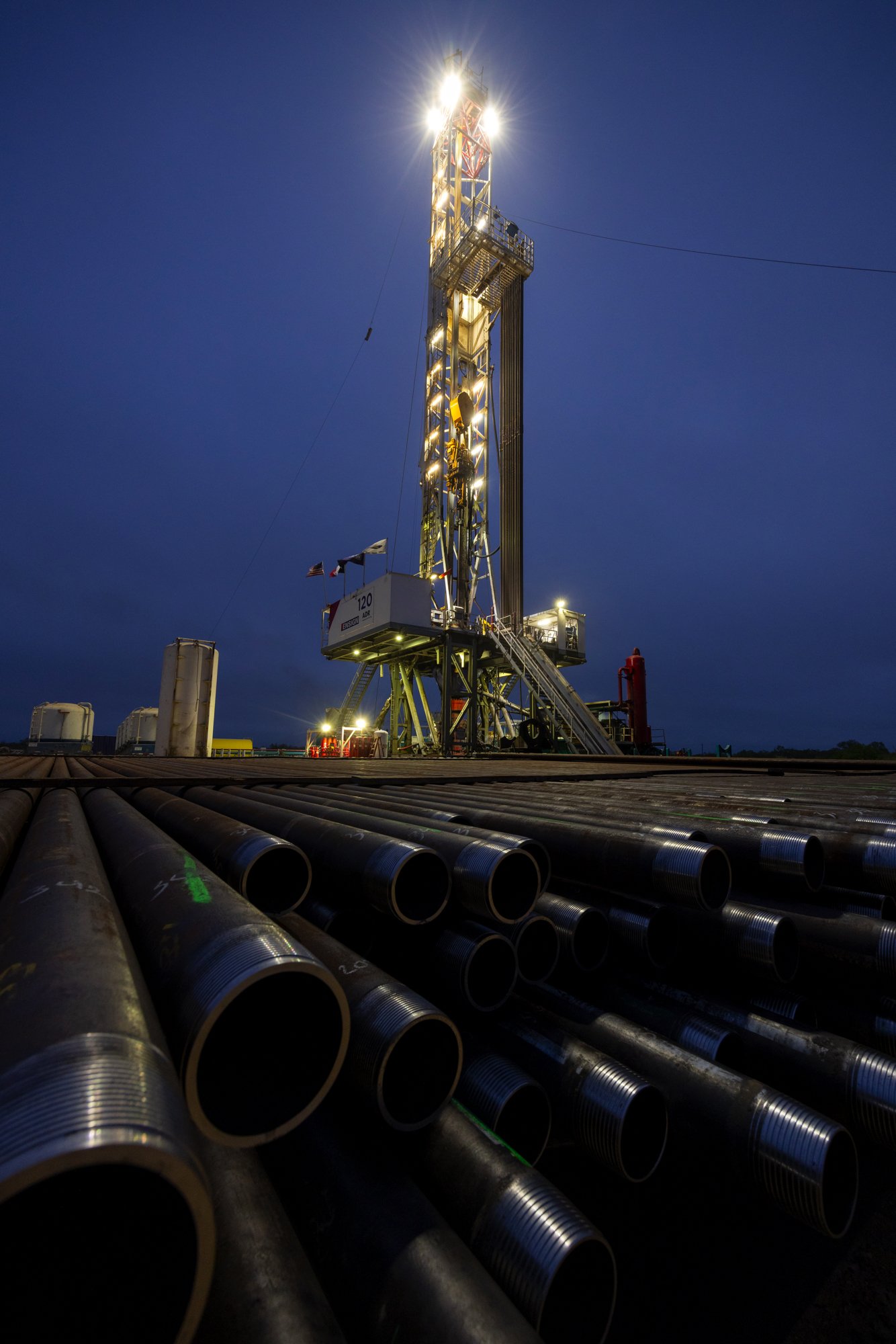Oil drilling rig with metal pipes in the foreground during dusk.