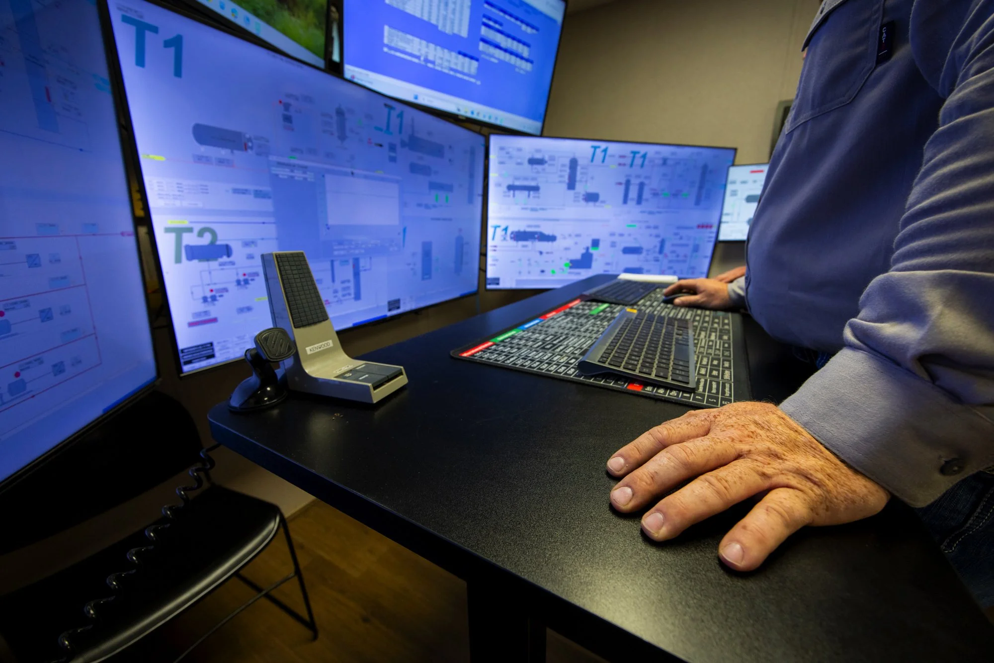 A person operating multiple computer screens displaying technical diagrams or schematics at a control station.