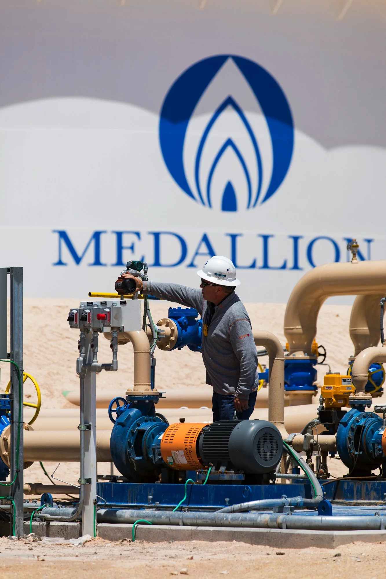 A worker wearing a white safety helmet and gray jacket inspecting machinery at a construction site with the Medallion logo in the background.