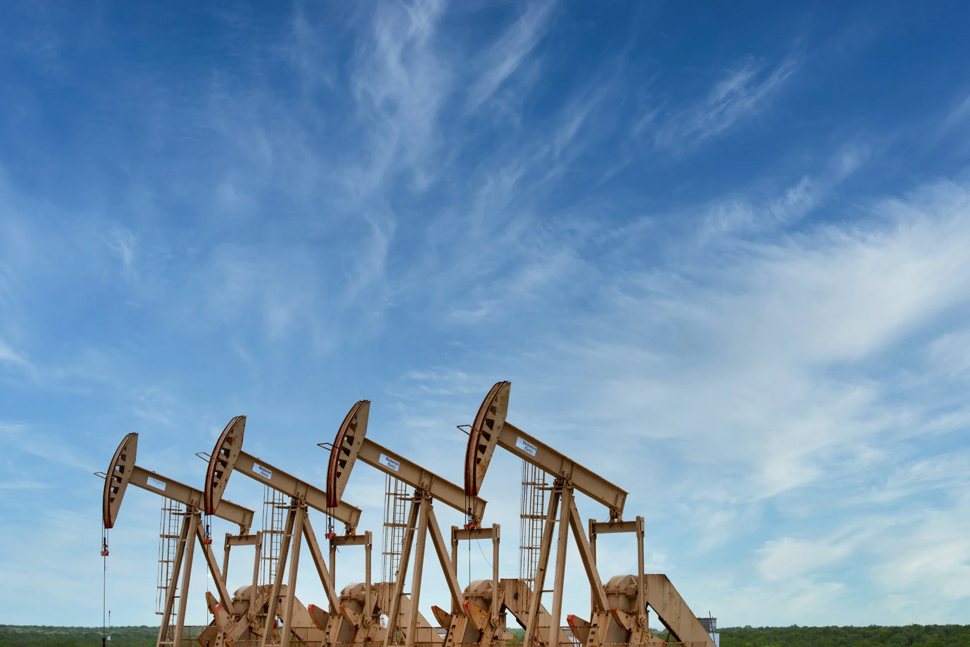 Multiple oil pumpjacks operating against a blue sky with wispy clouds.