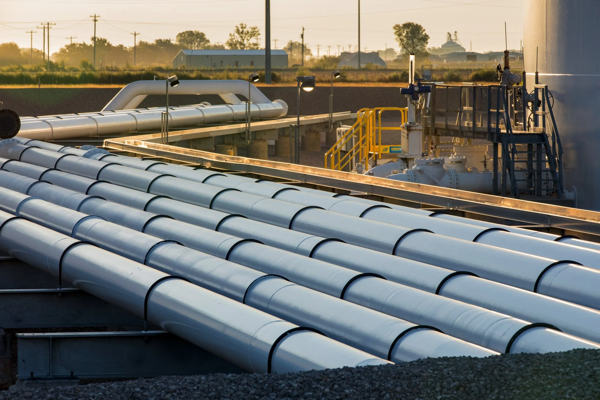 Industrial pipelines and valves at an industrial site during sunset.
