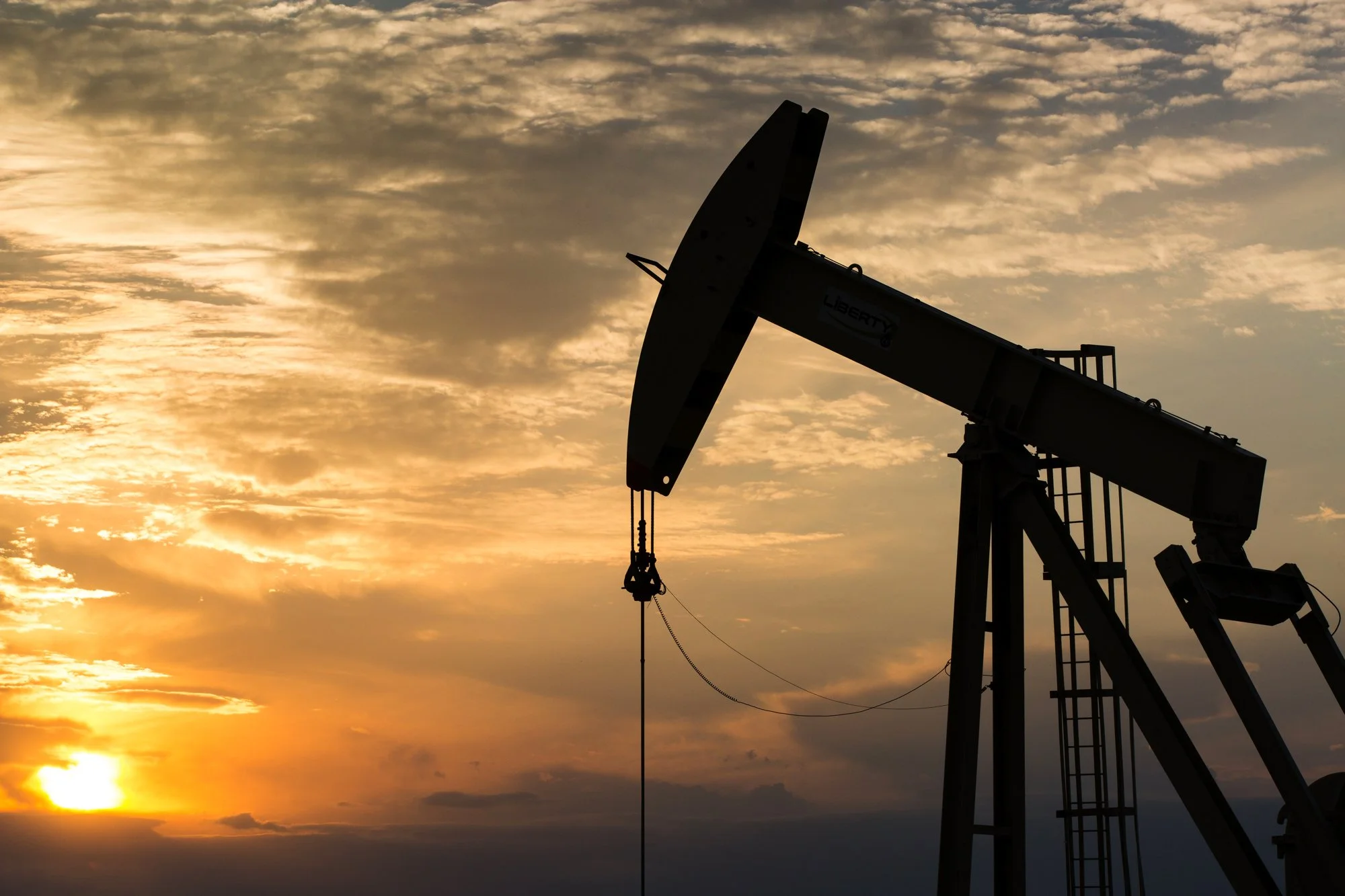 Silhouette of an oil pumpjack against a sunset sky.
