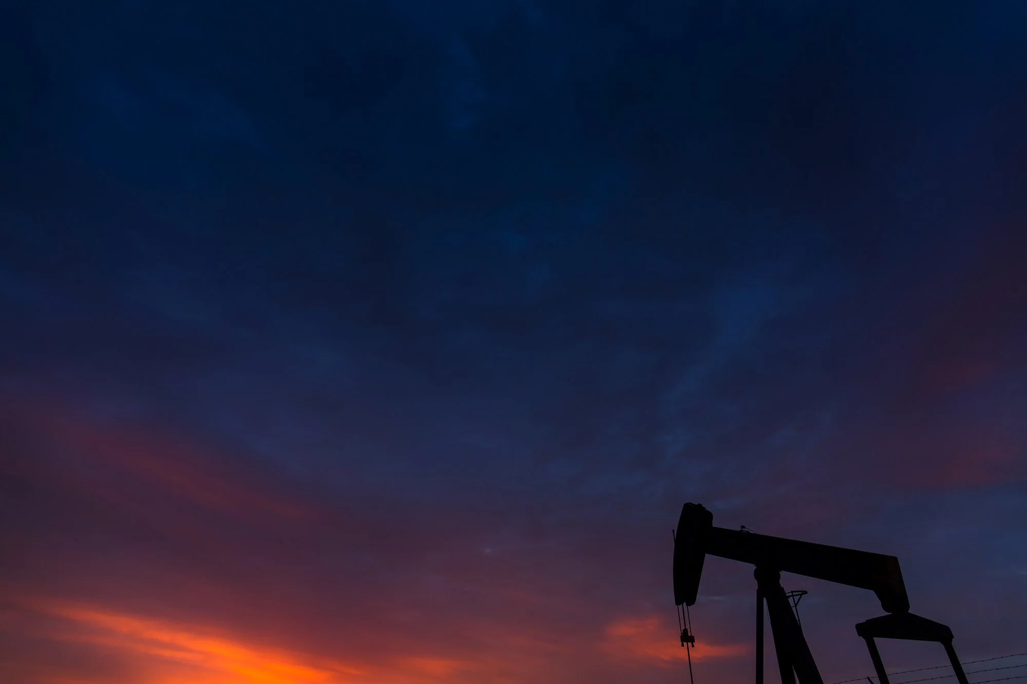 Silhouette of an oil pumpjack against a colorful sunset sky with blue and orange hues.