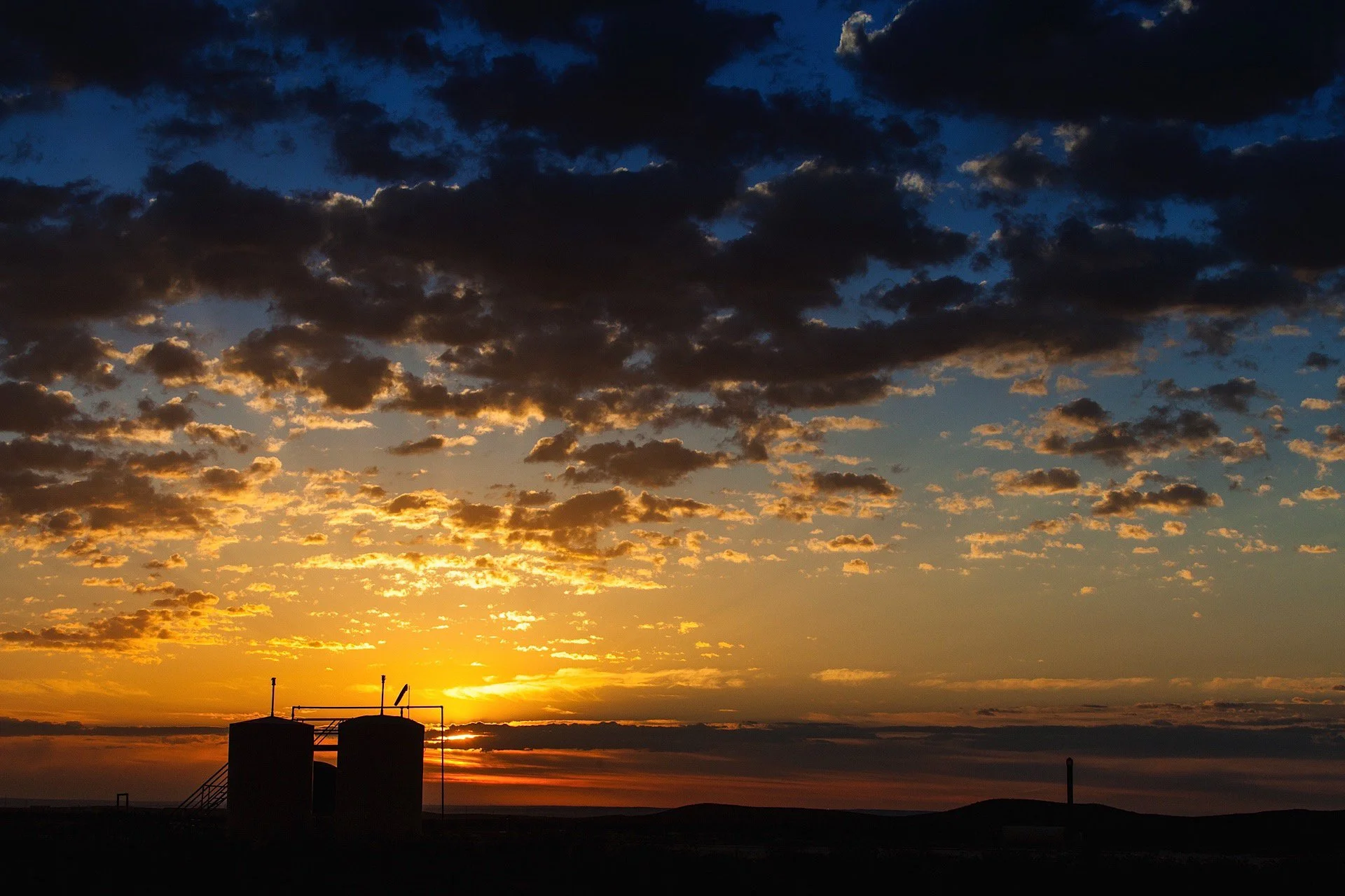 Sunset with clouds and silhouettes of industrial tanks on the horizon.