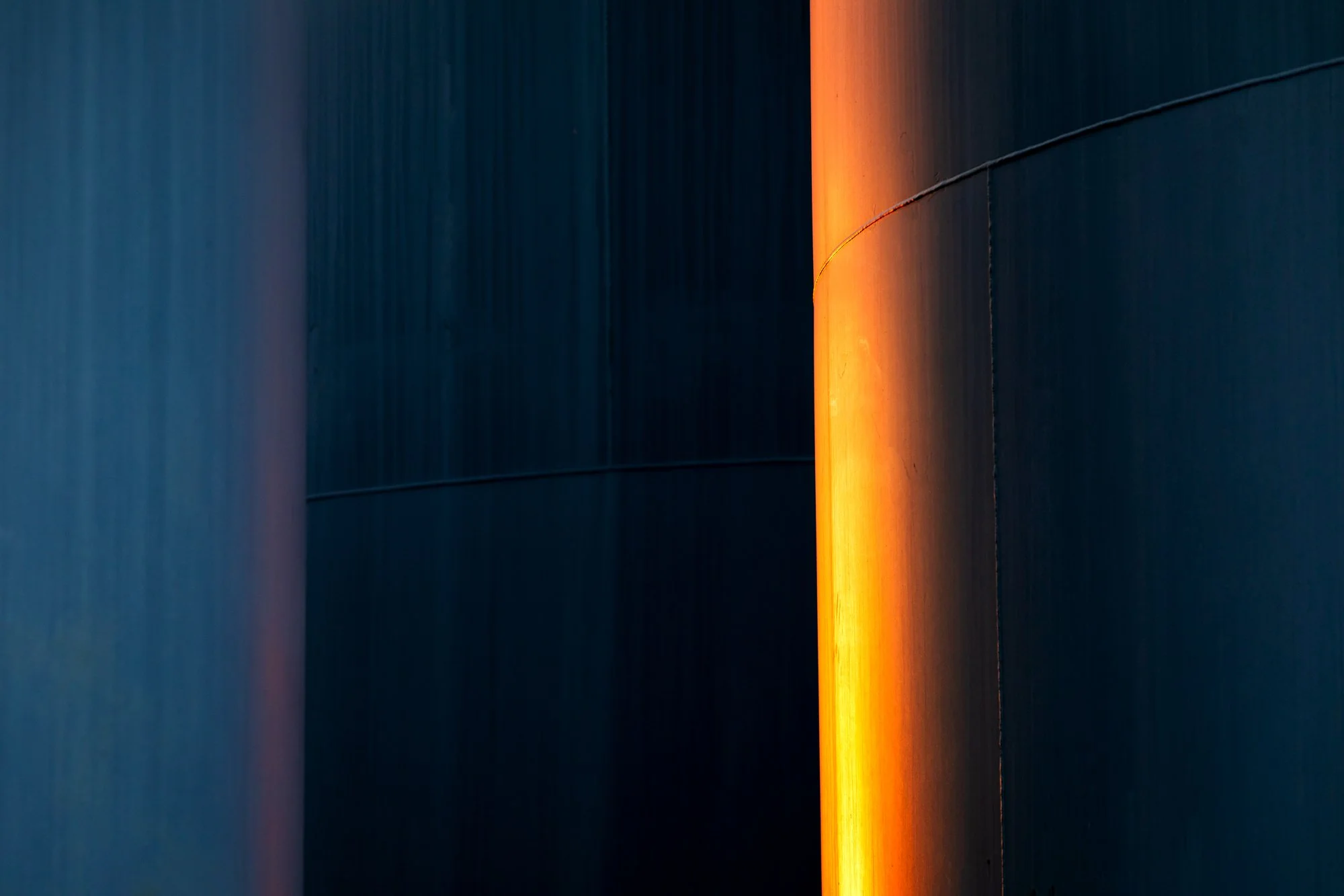 Close-up of a modern building's exterior wall with a vertical strip of orange light contrasting against dark blue panels.