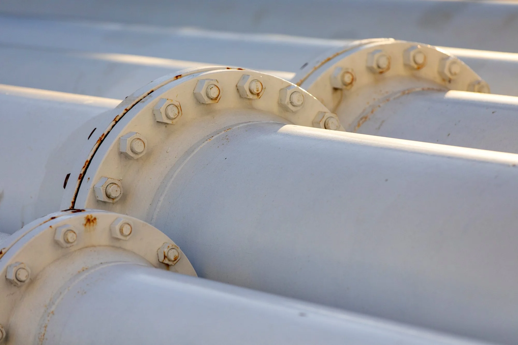Close-up of white industrial pipes with flanges and bolts, showing some rust spots.