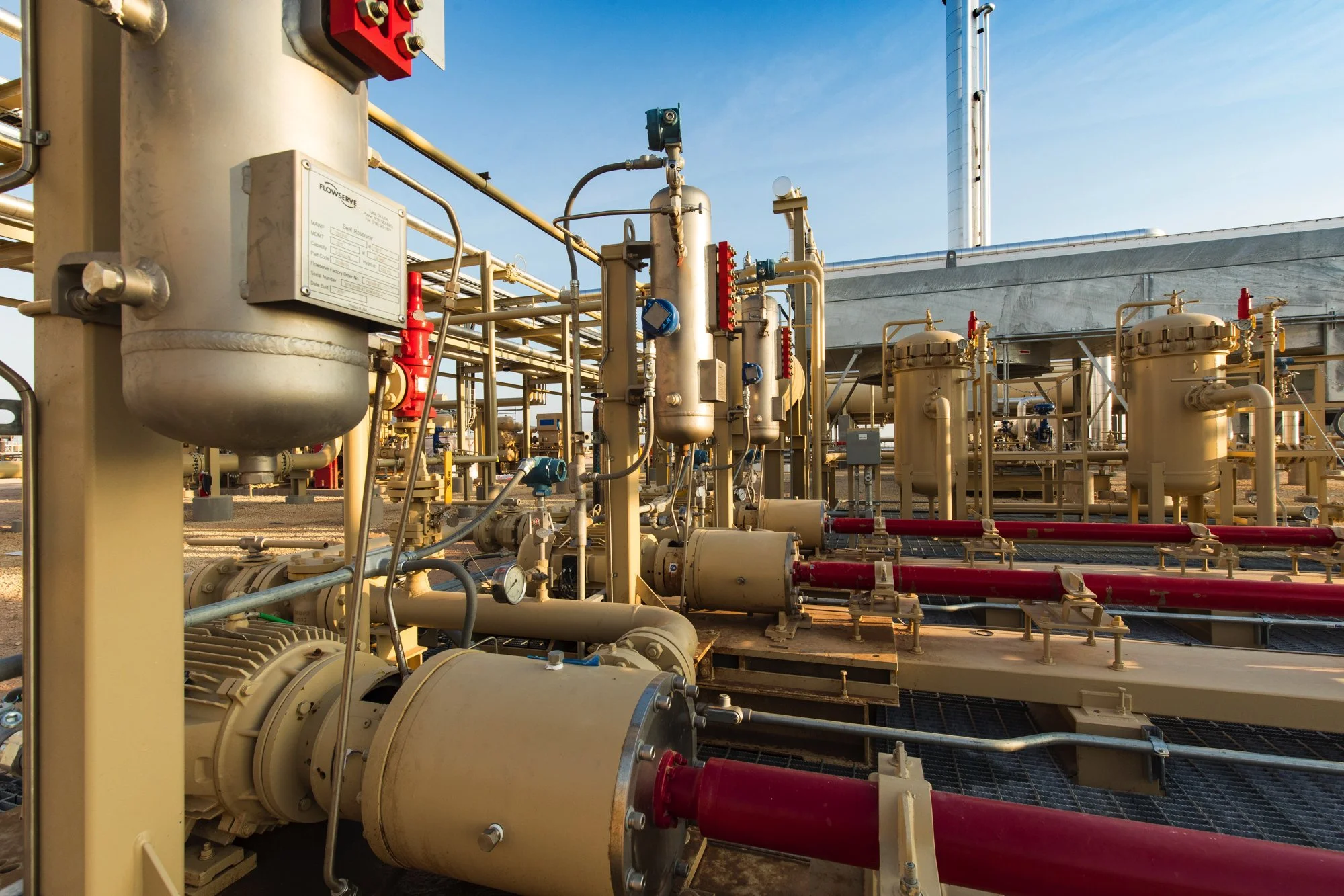 Industrial facility with pipes, tanks, and machinery under a blue sky.