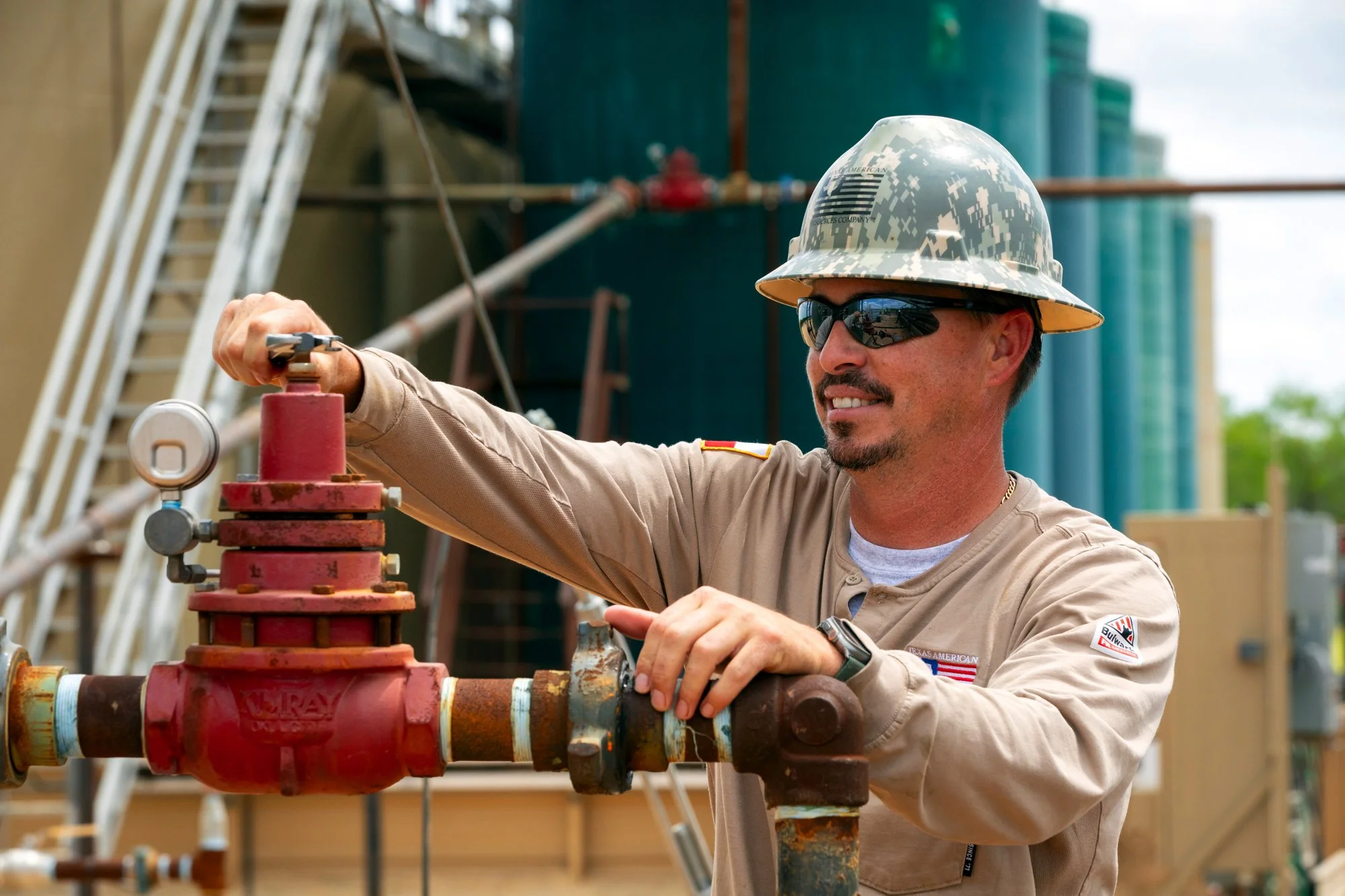 Pipeline worker wearing safety helmet and sunglasses adjusting a valve at a construction site.