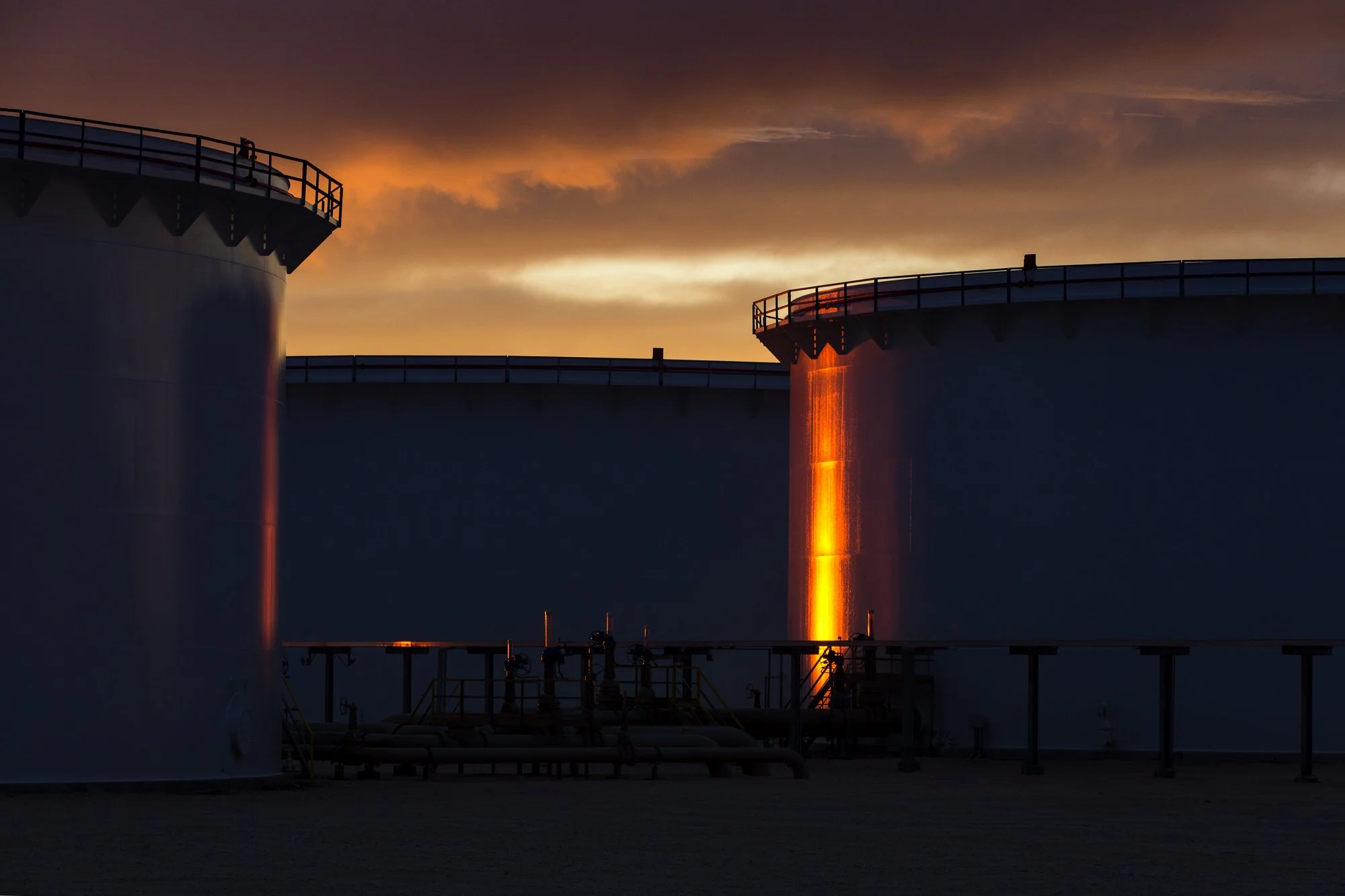 Industrial tanks illuminated by the sunset with cloudy sky in the background.