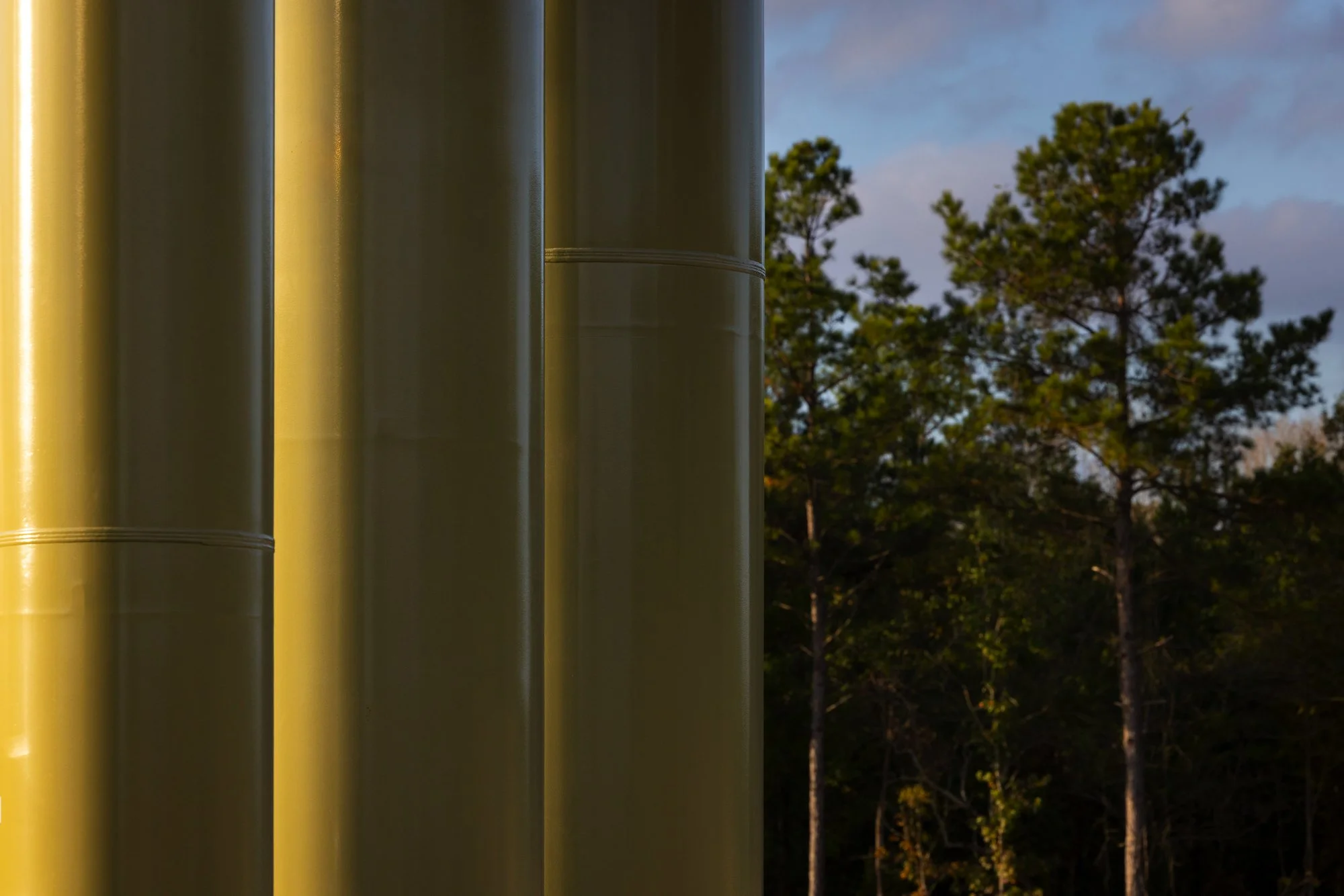 Close-up of yellow metal pipes on the left side with trees and sky in the background.