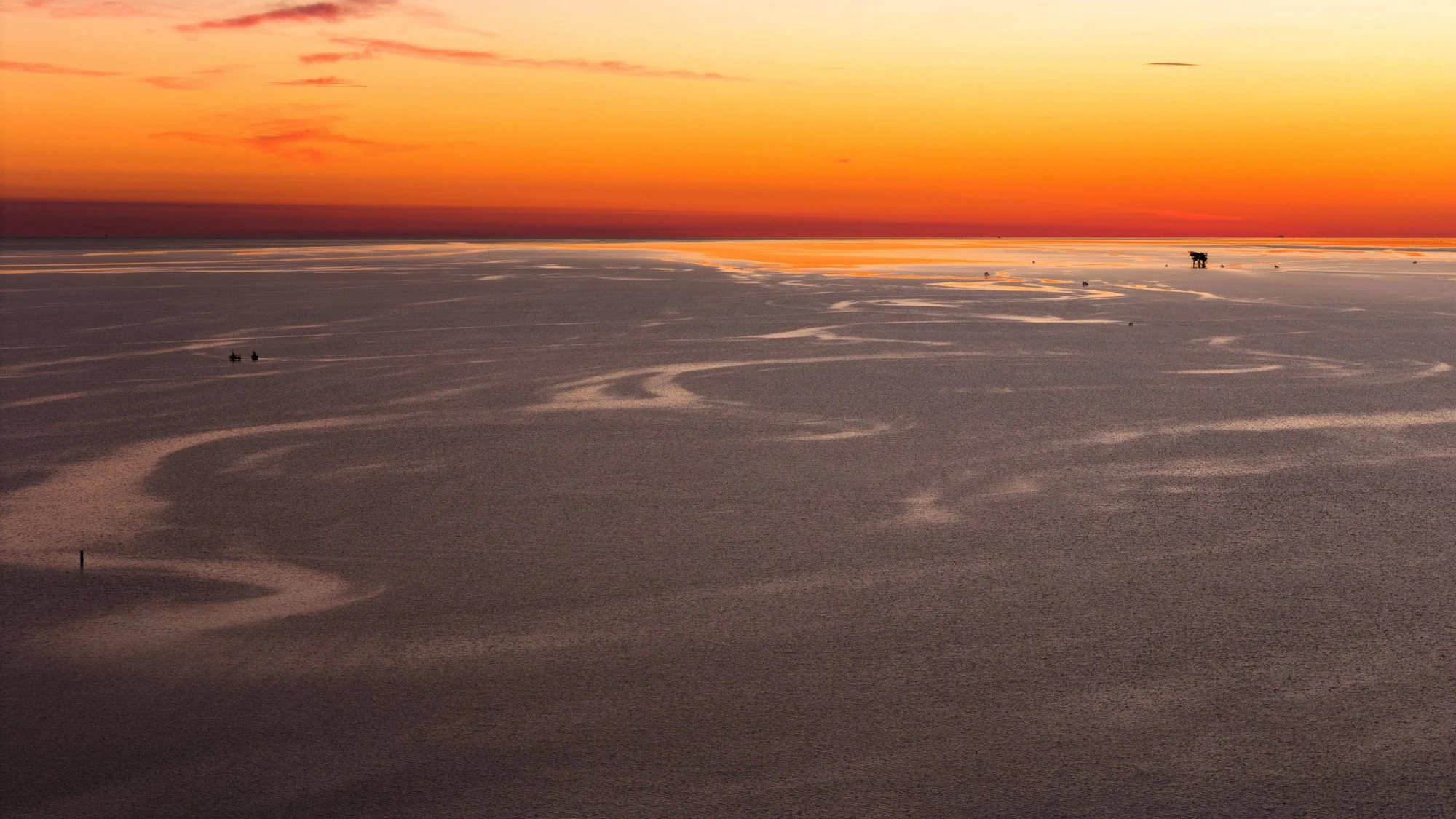 Salt flats at sunset with boats in the distance, colorful sky and long salt formations.