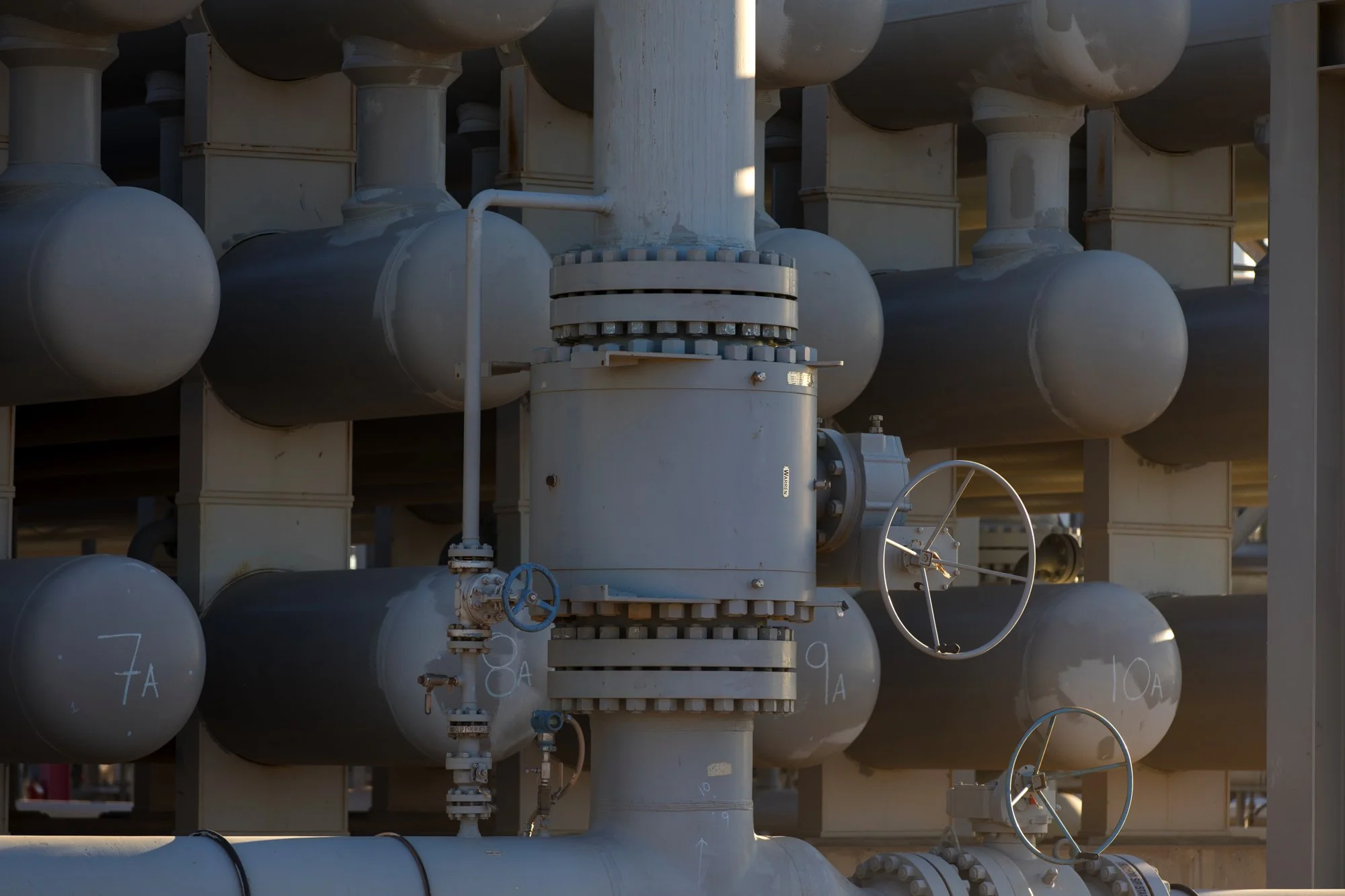 Industrial pipes and valves painted in gray, labeled with numbers, part of a large pipe system.